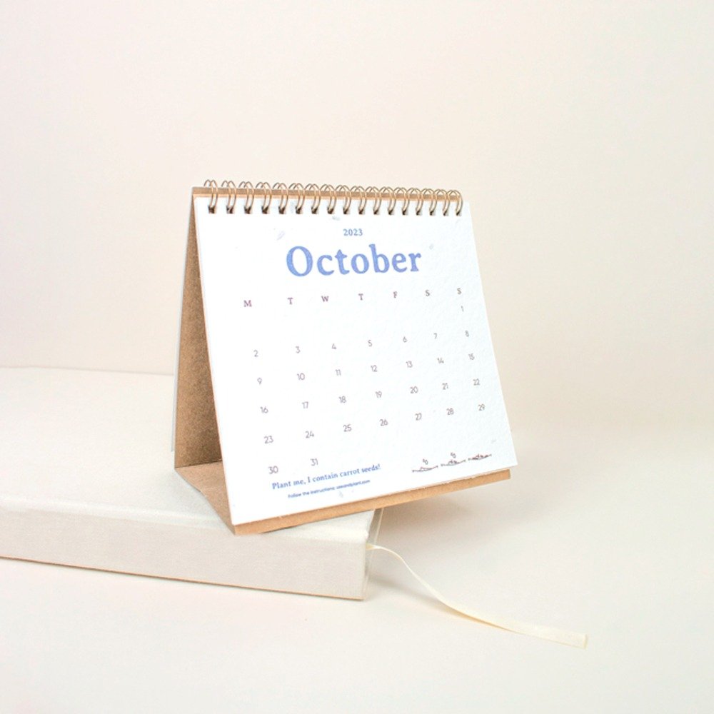 Calendario de papel plantable triangular abierto en el mes de octubre sobre un cuaderno blanco