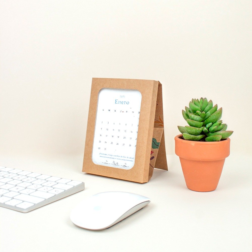 Calendario de papel plantable ecológico con soporte en papel kraft junto a un cactus, un teclado y un ratón de ordenador