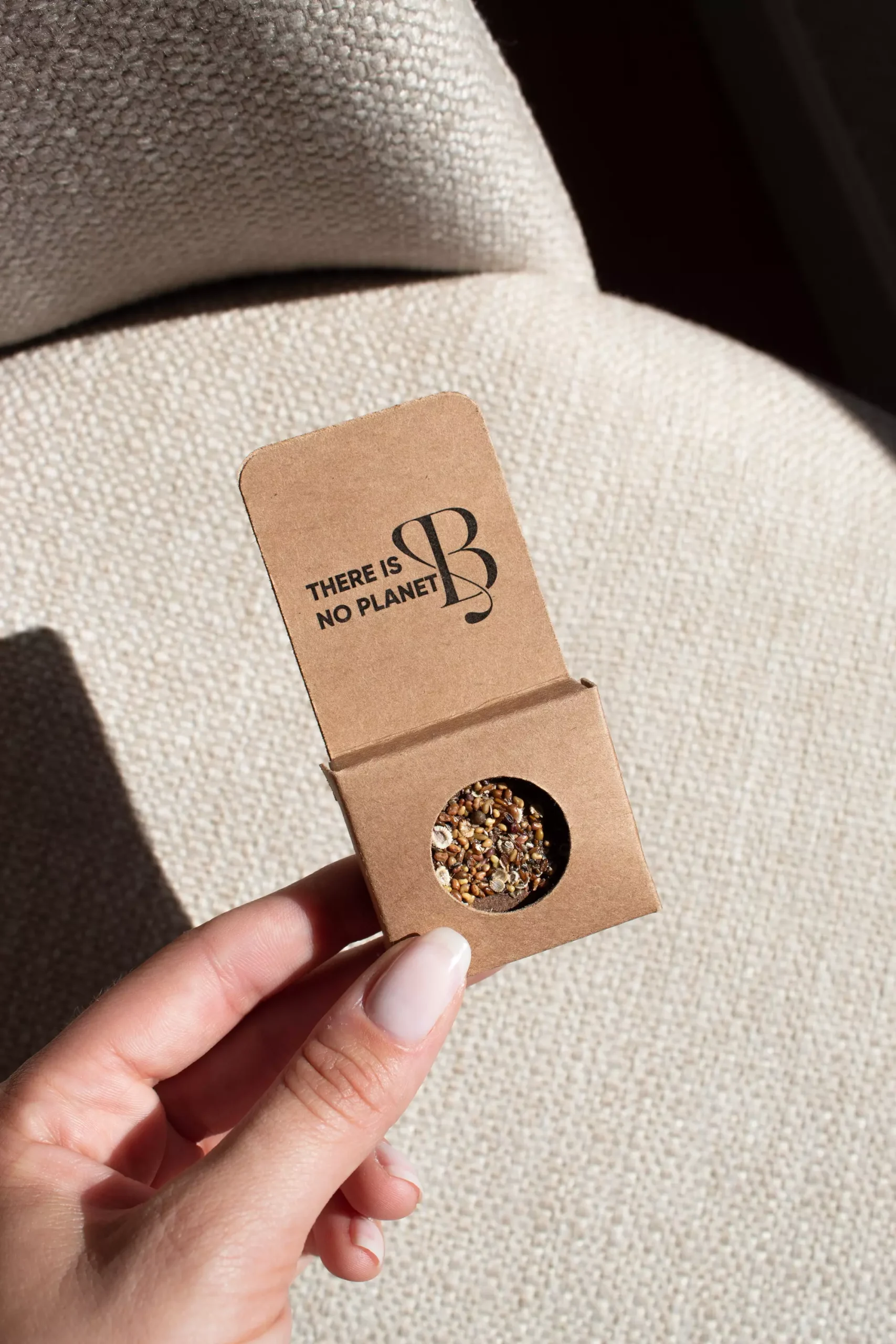Mano sujetando una bomba de semillas dentro de un packaging de cartón kraft personalizado 