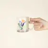 Mano de mujer sujetando una taza de cristal personalizada con logo de colores
