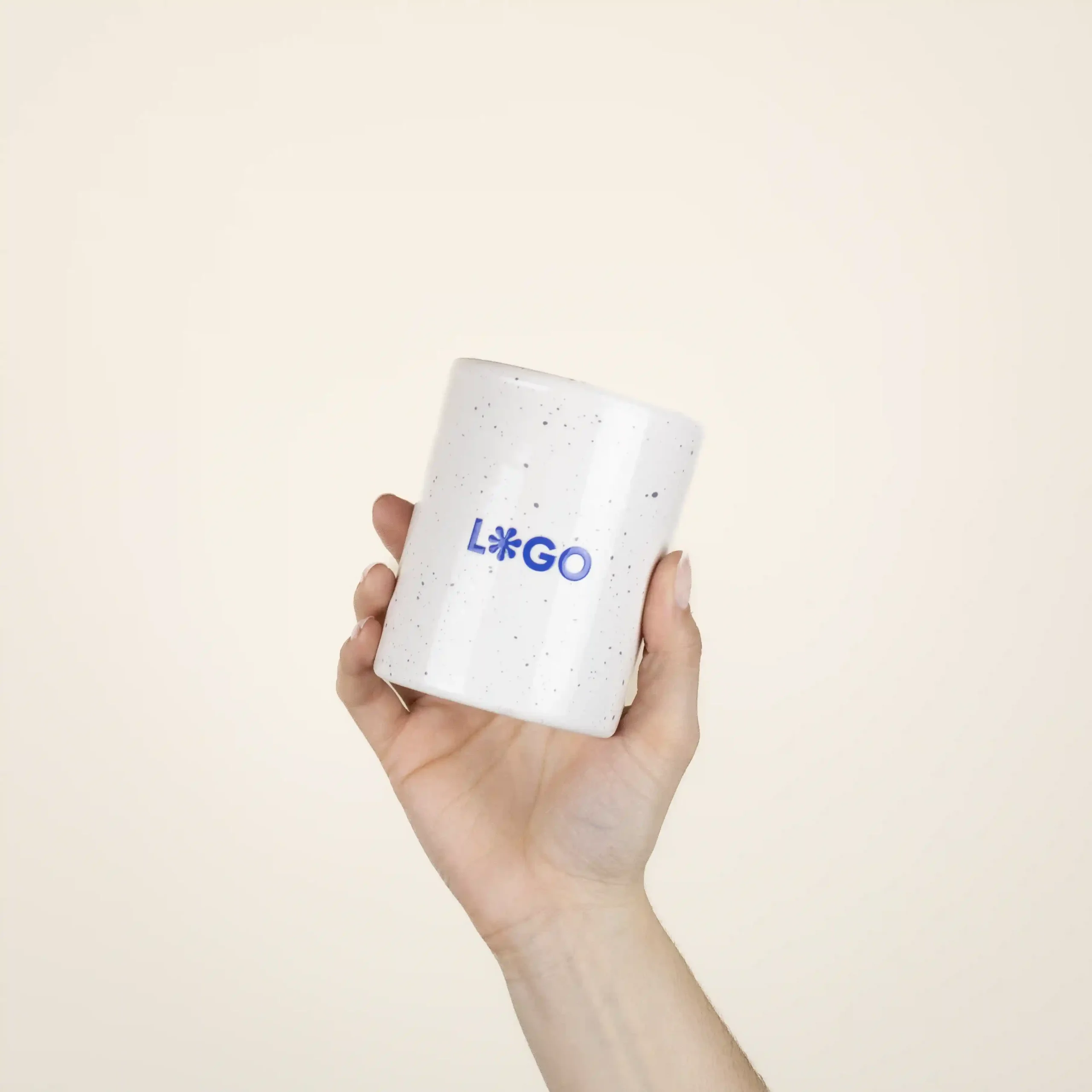 Taza de cerámica CANDELA Mano mostrando una taza de cerámica blanca con puntos negros personalizada con la palabra logo en azul