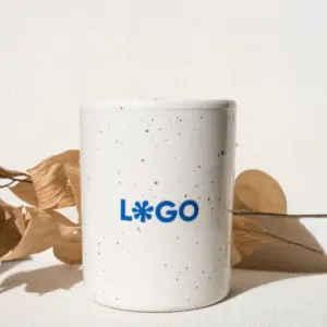 Taza de cerámica blanca con puntos negros personalizada con logo azul delante de una rama de hojas secas