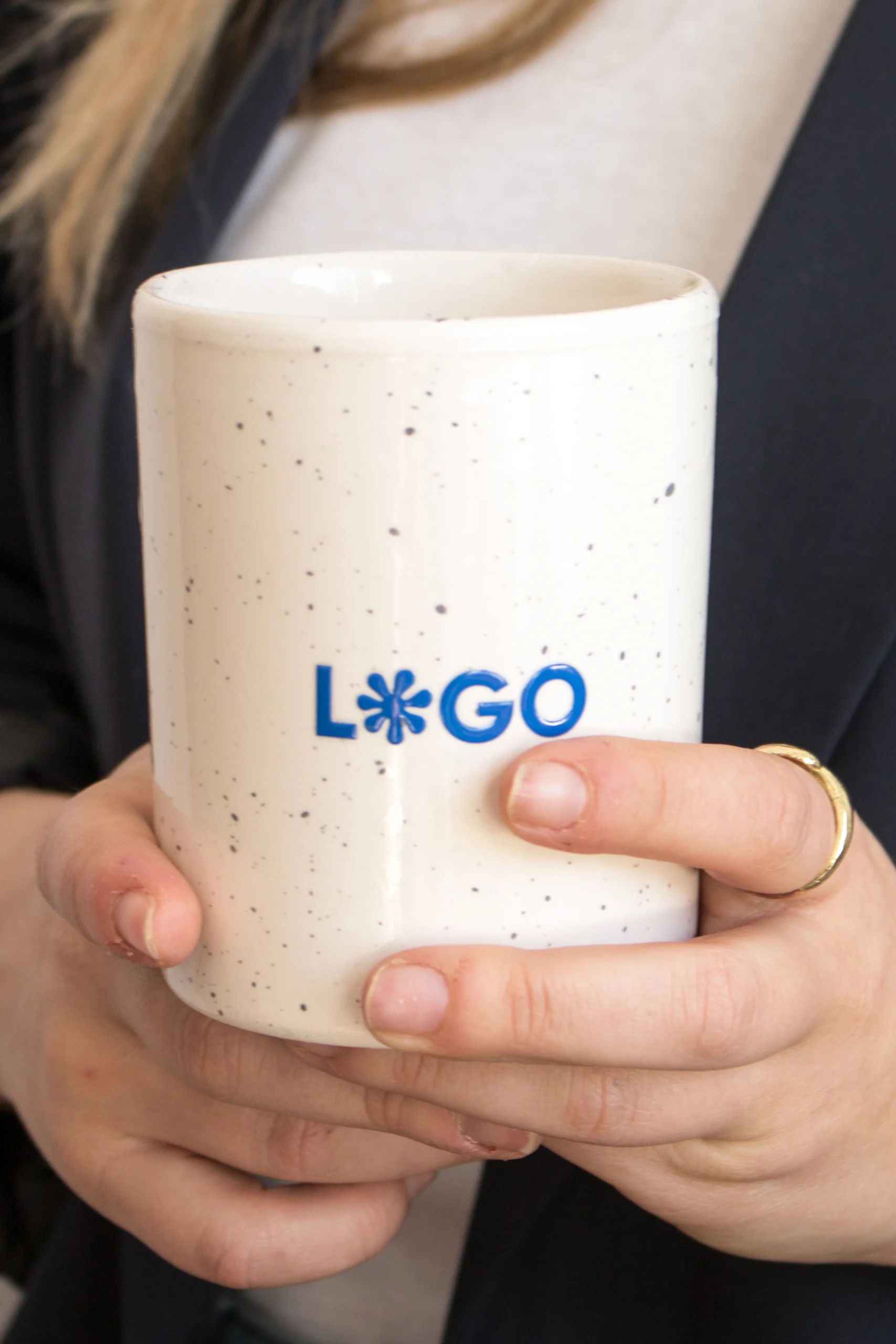 Manos sujetando una taza de cerámica blanca con puntos negros personalizada con logo azul
