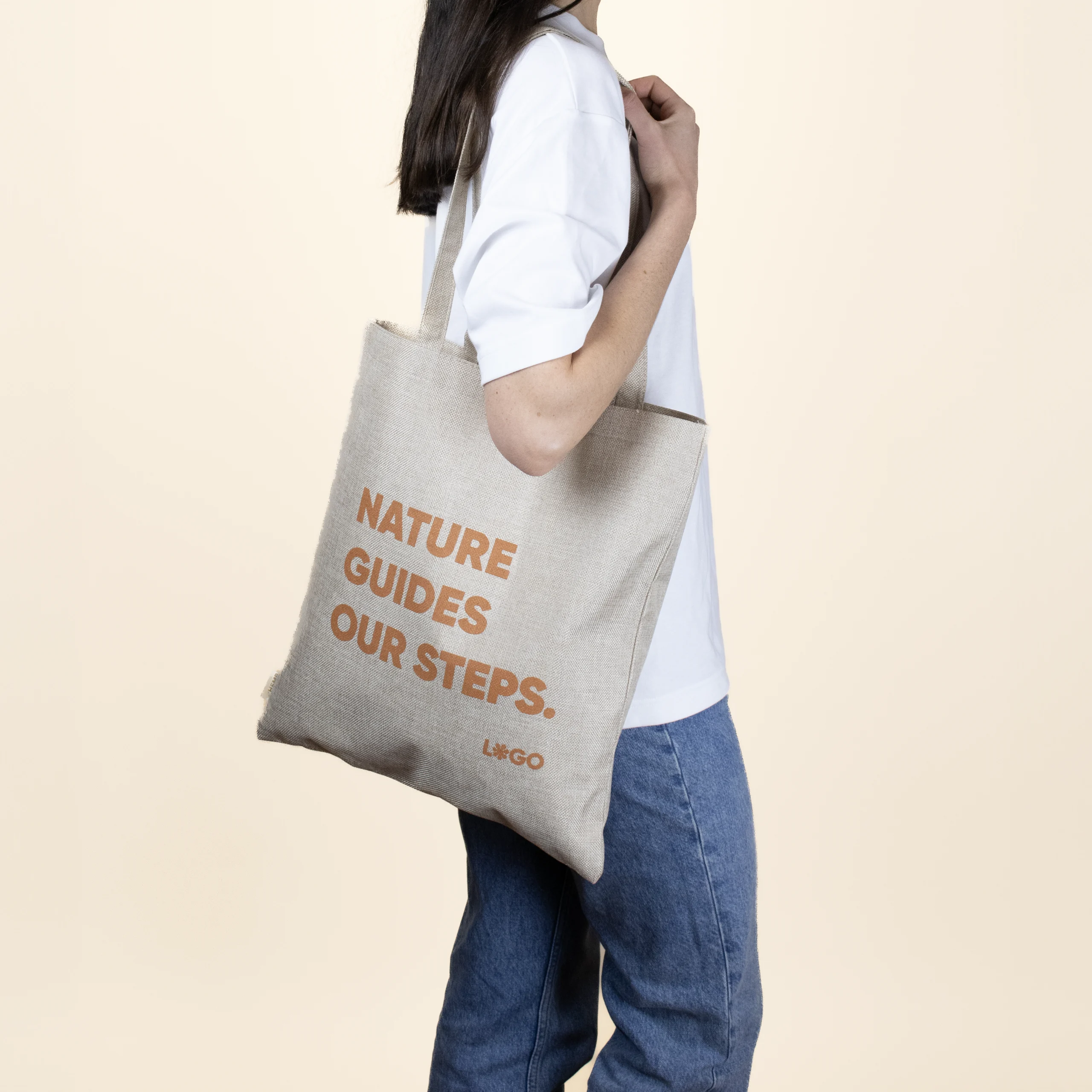 Chica posando sobre fondo beige con bolsa de cáñamo personalizada con logo naranja