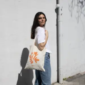 Chica paseando en la calle llevando una bolsa de algodón personalizada con logo naranja