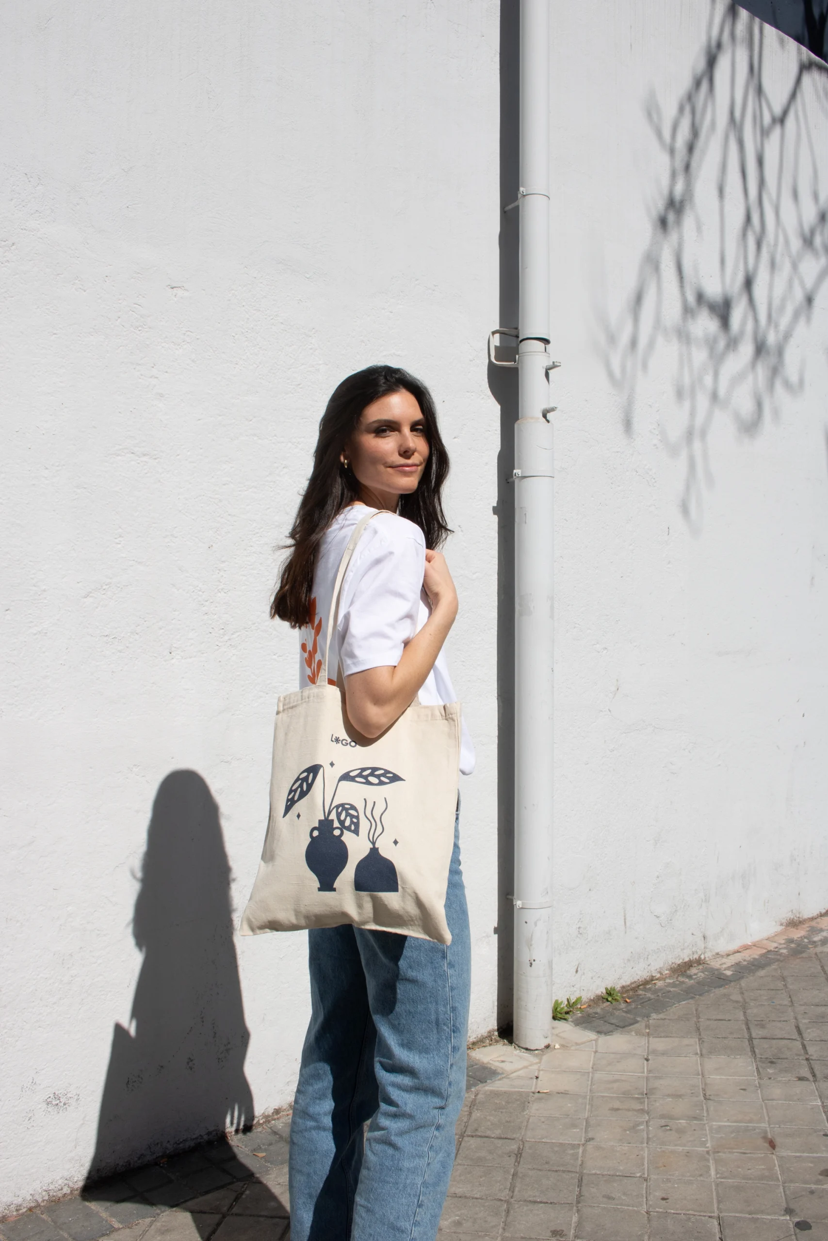 Chica paseando en la calle llevando una bolsa de algodón personalizada con logo azul