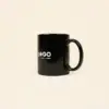 Taza negra personalizada IRIS Taza negra con asa personalizada con la palabra logo en blanco fotografiada sobre un fondo beige
