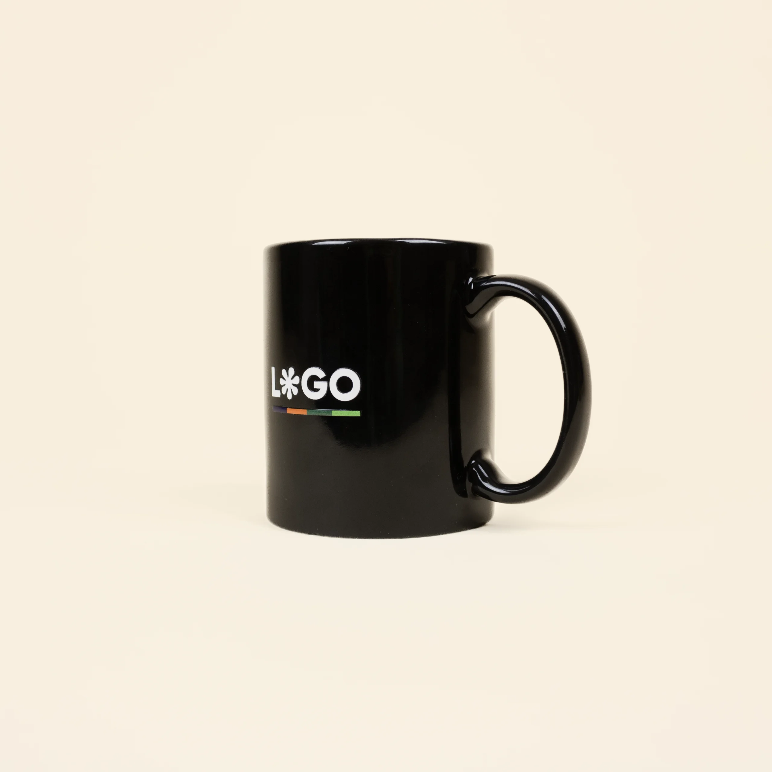 Taza negra personalizada IRIS Taza negra con asa personalizada con la palabra logo en blanco fotografiada sobre un fondo beige