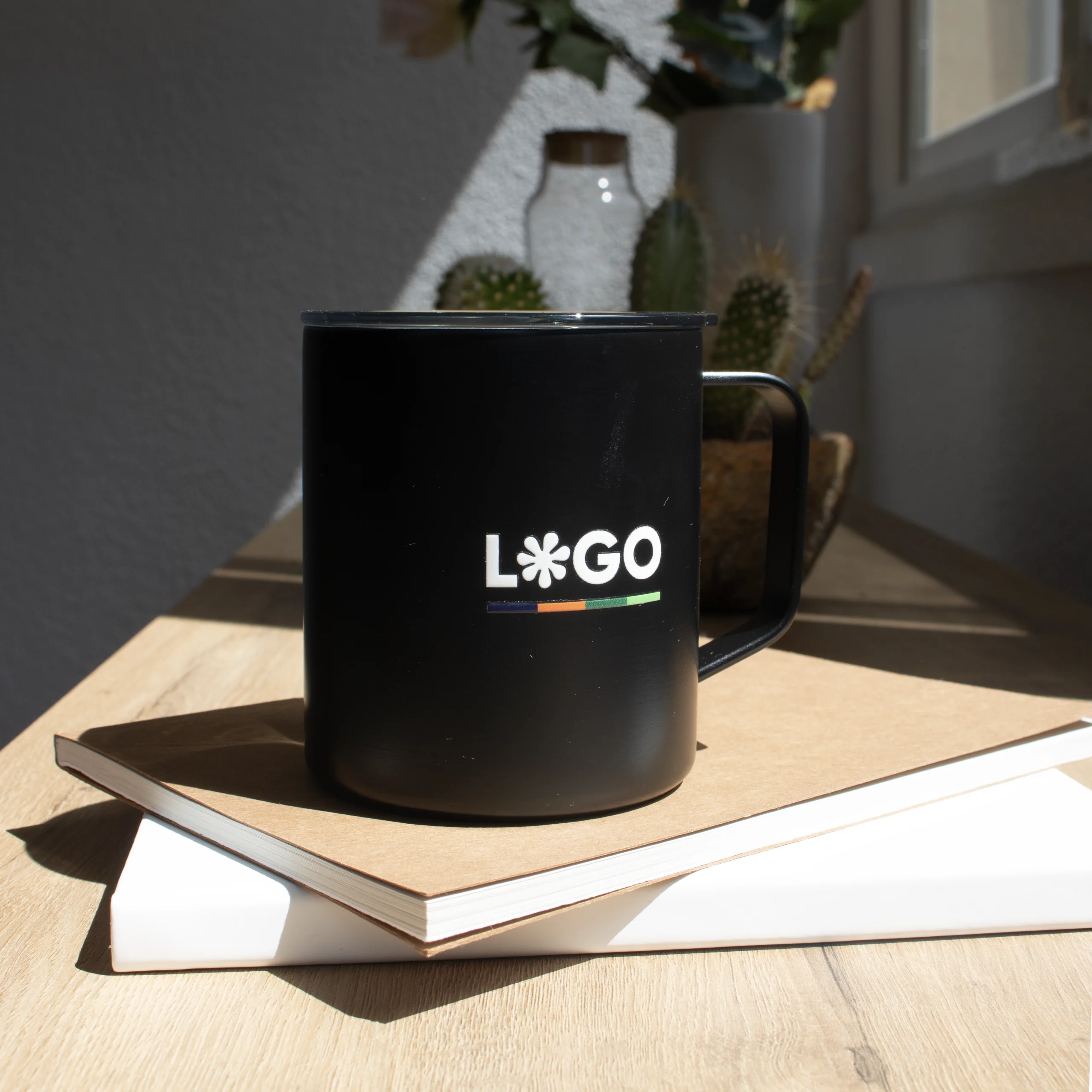Vaso térmico con asa negro con logo blanco apoyada en cuadernos