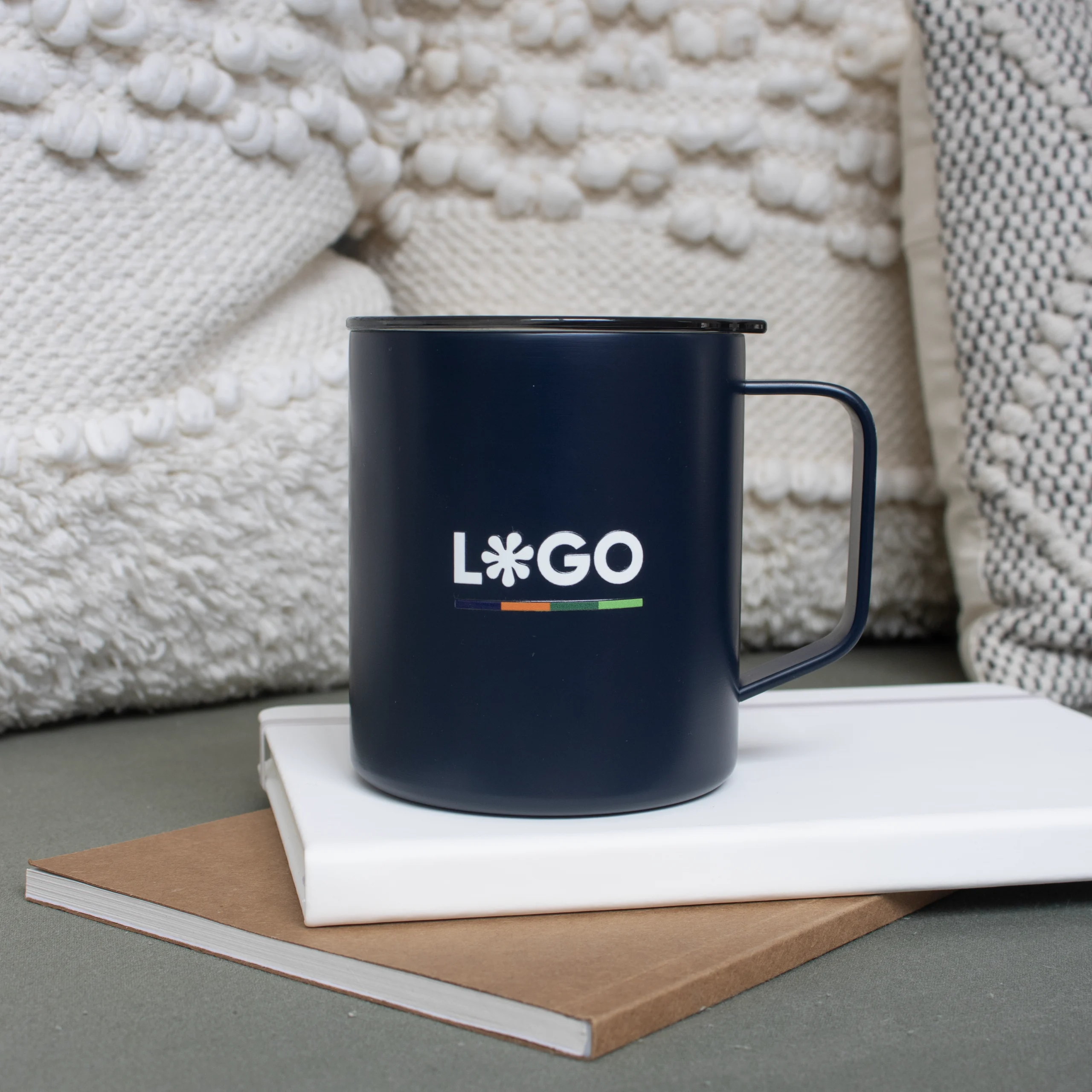 Vaso térmico con asa azul con logo blanco apoyada en cuadernos