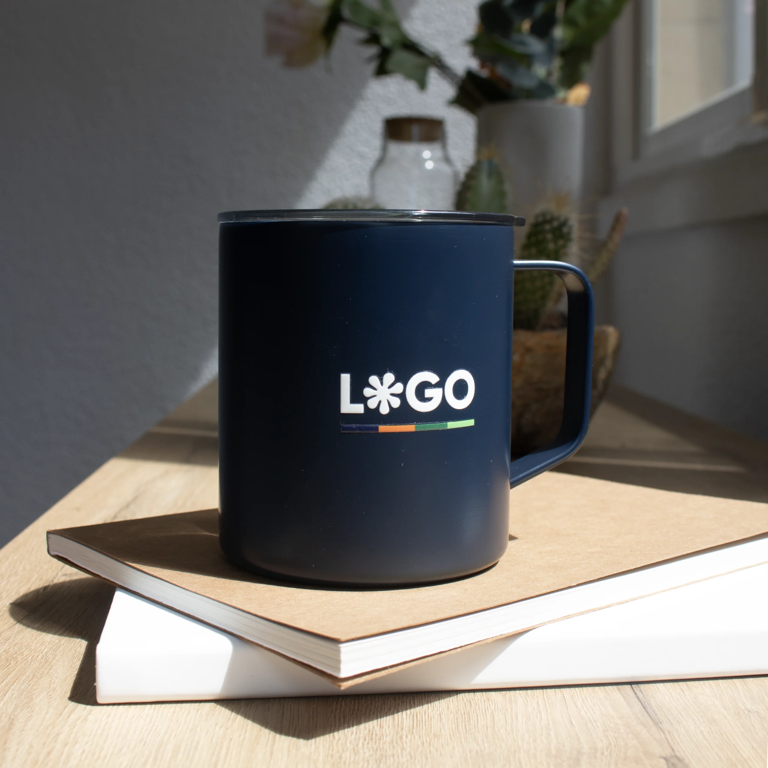 Vaso térmico con asa azul con logo blanco apoyada en cuadernos
