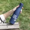 Mano cogiendo una botella azul de acero inoxidable personalizada con logo blanco