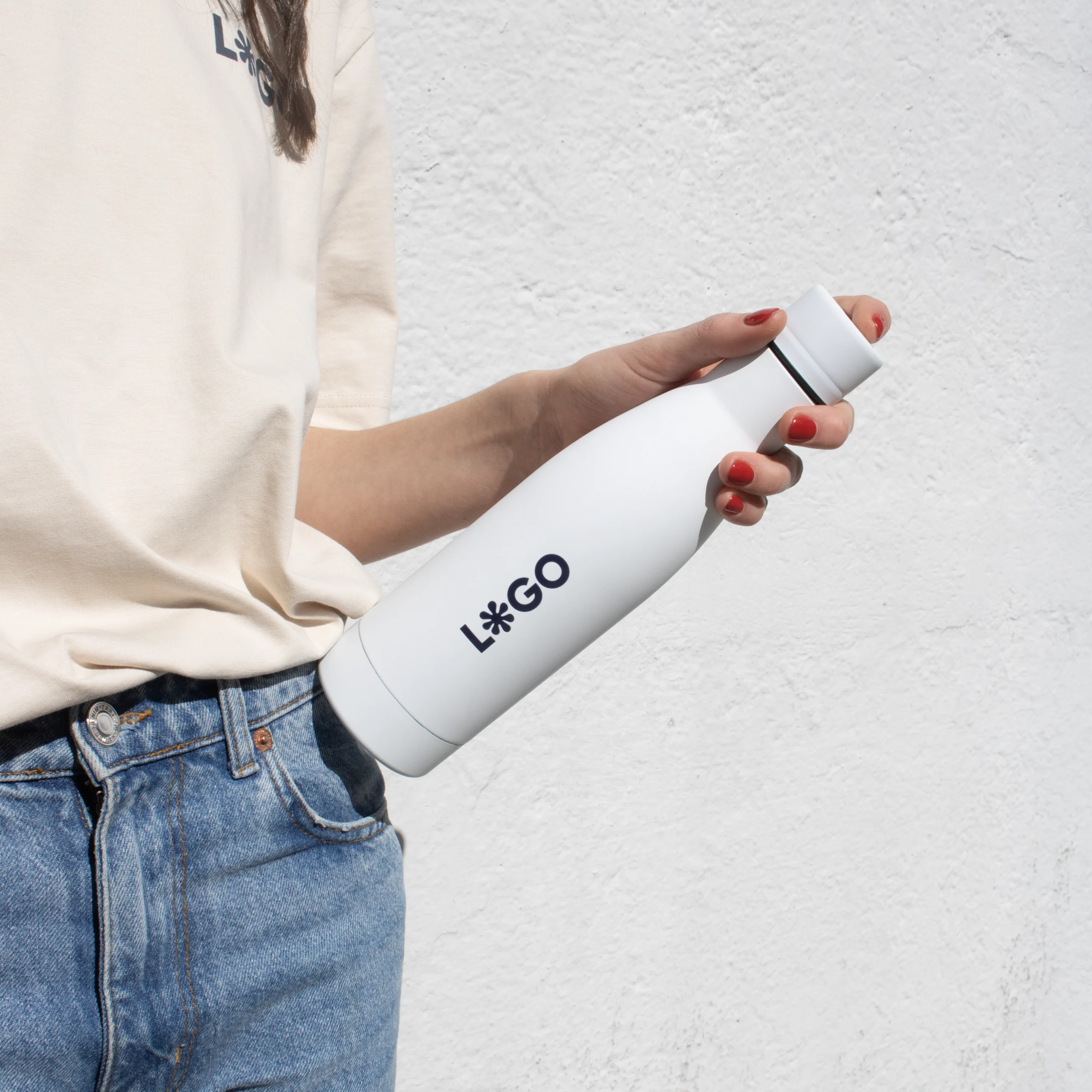 Chica en vaqueros y camiseta beige sujetando con la mano una botella blanca de acero inoxidable personalizada con logo azul