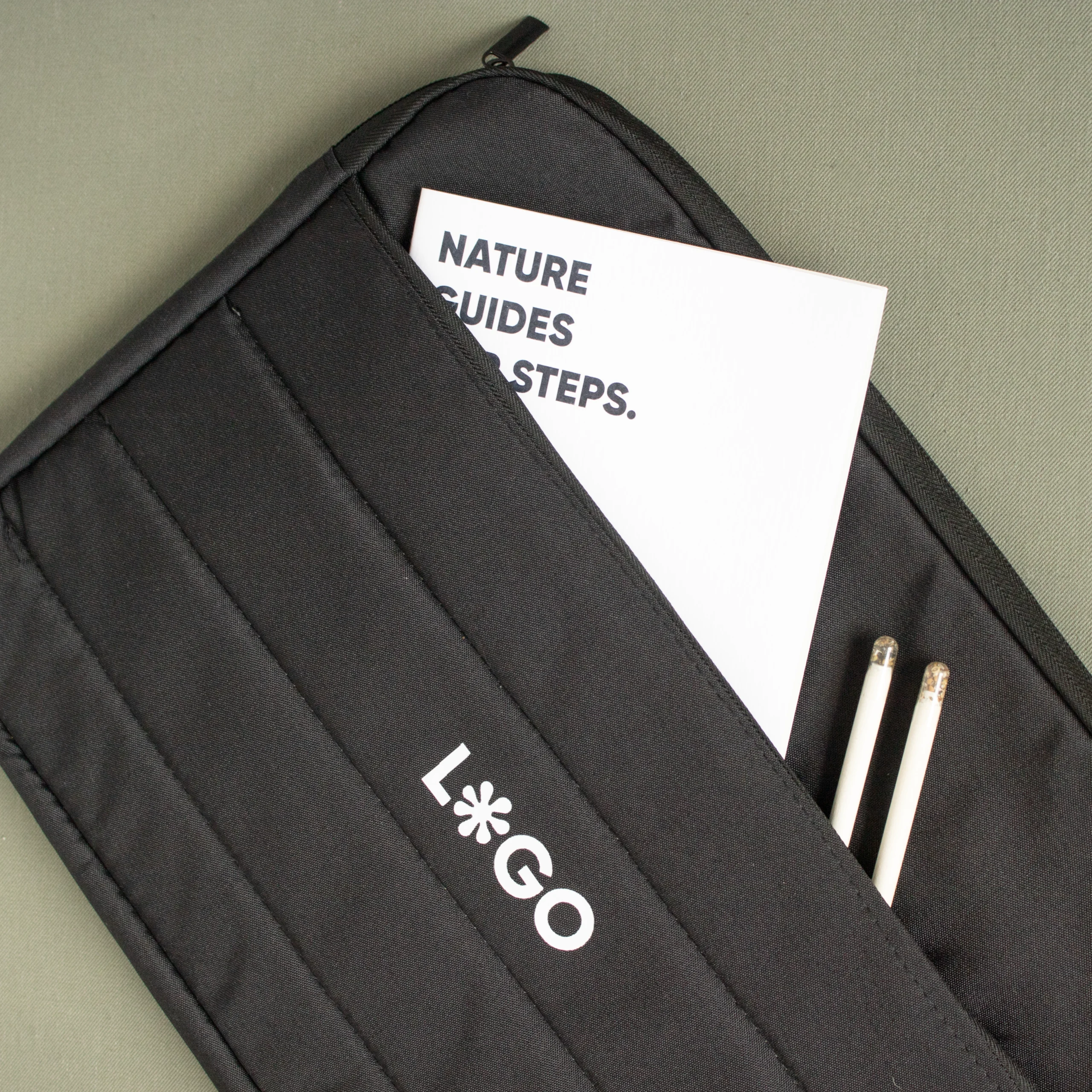 Funda portátil negra personalizada con logo blanco cuaderno blanco y lápices fondo verde