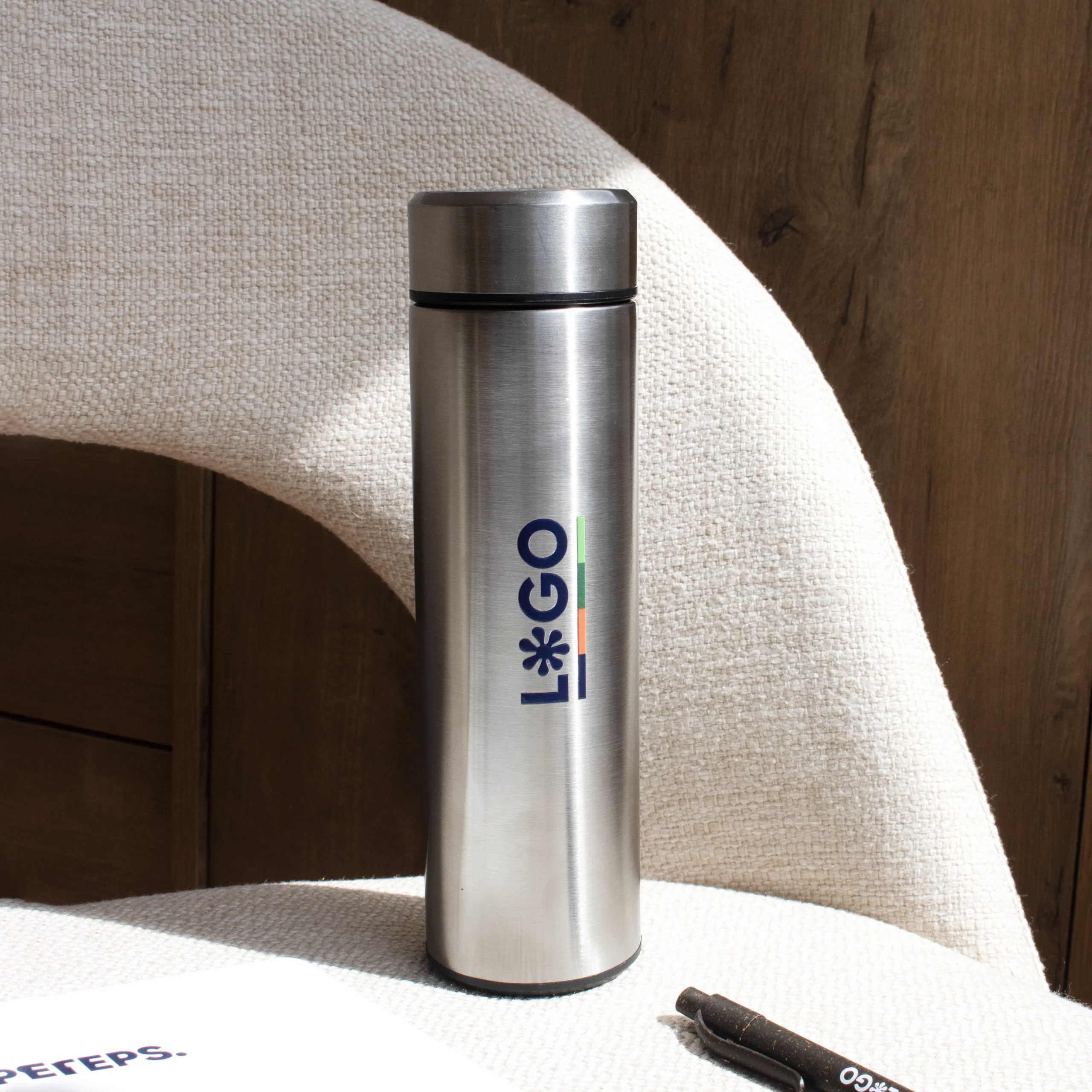 Termo acero inoxidable personalizado plateado logo azul apoyado en silla gris