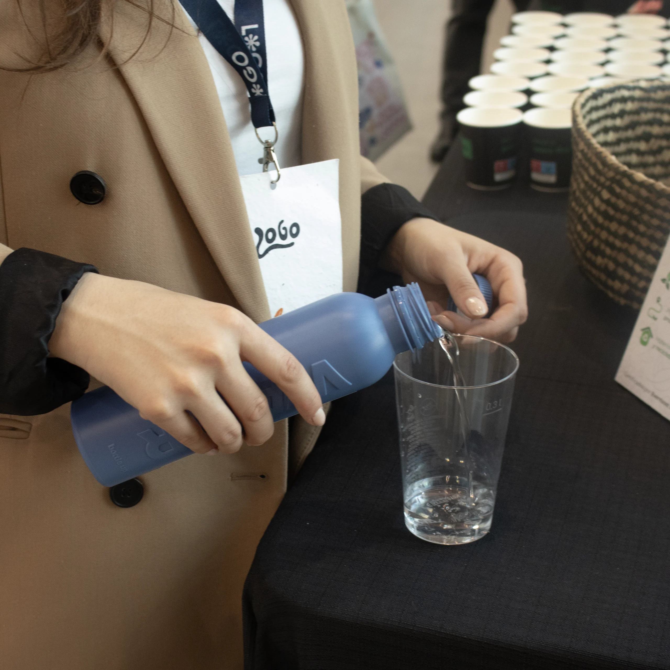 Chica echando agua a un vaso de una botella azul de caña de azúcar personalizada en un evento de empresa