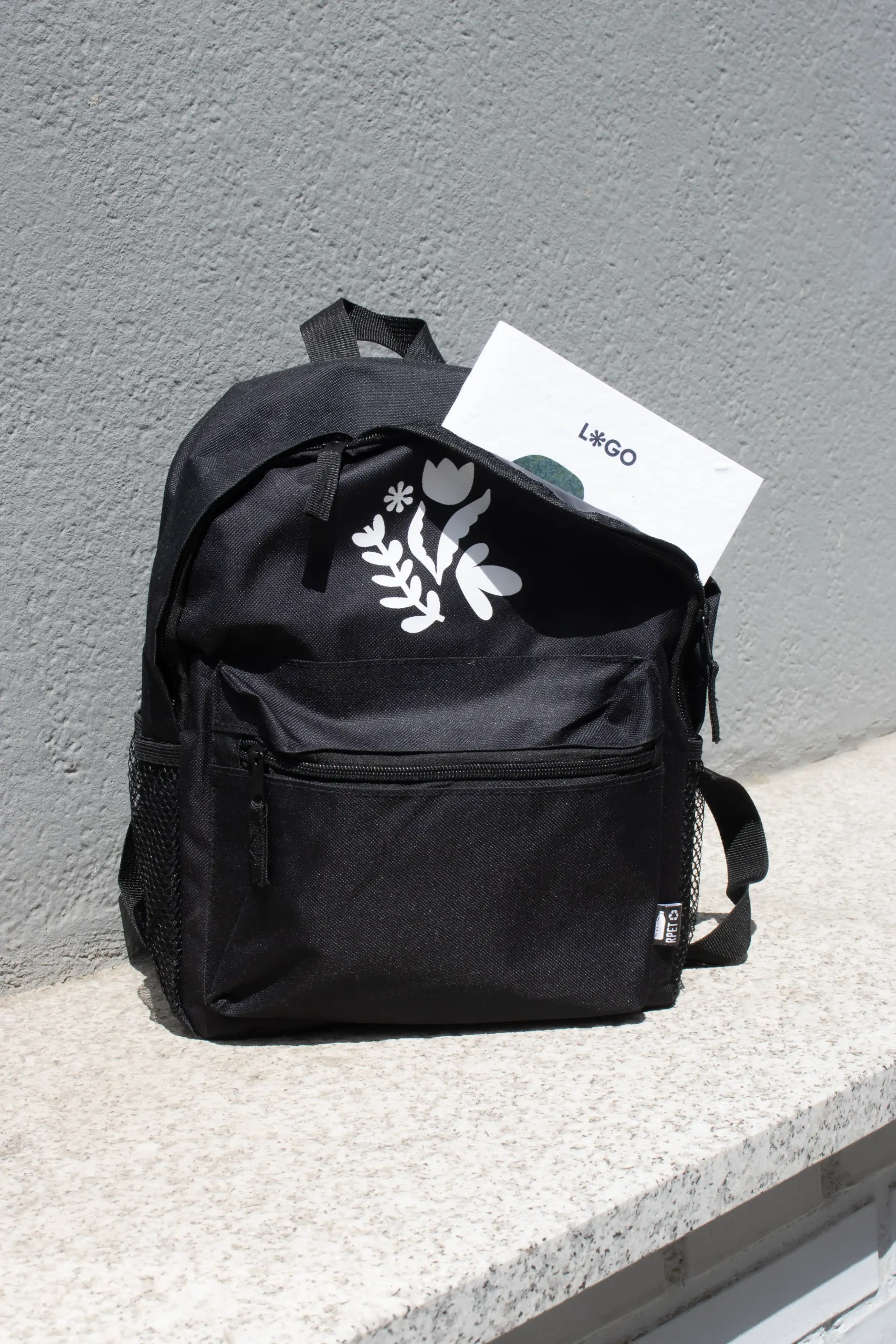 Sac à dos personnalisé pour enfants de couleur noire avec logo blanc et cahier blanc à fond gris