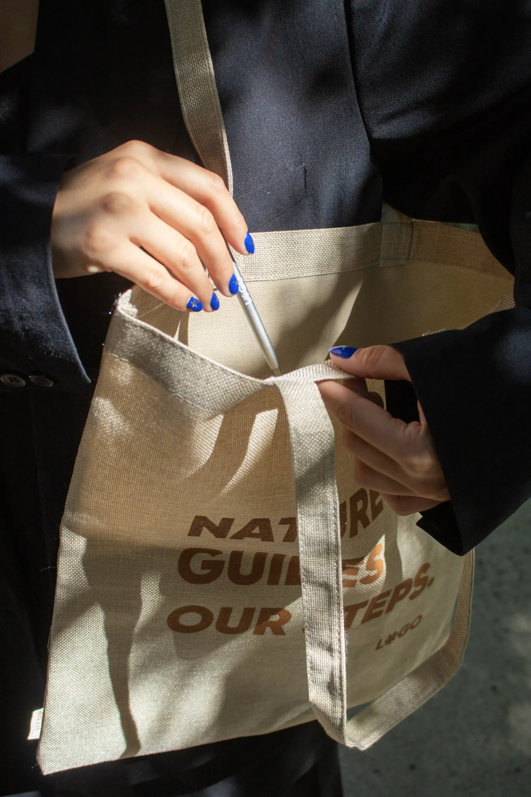 Manos introduciendo un bolígrafo de aluminio en una tote bag