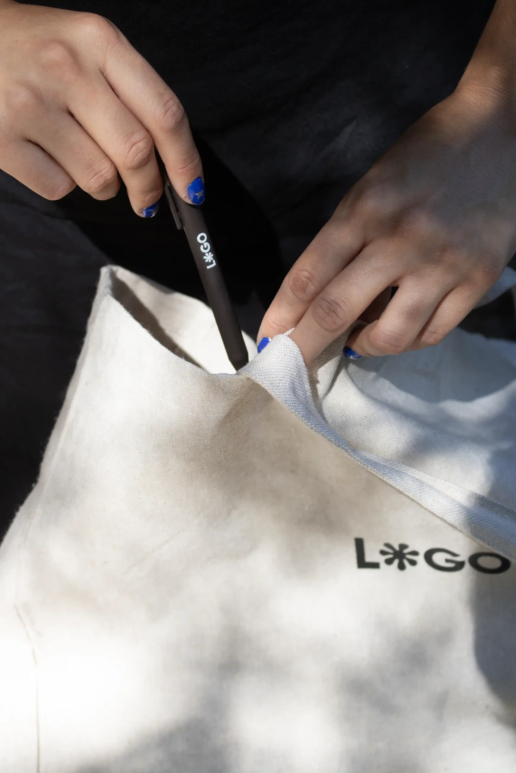Manos introduciendo un bolígrafo de fibra de café personalizado en una tote bag de algodón