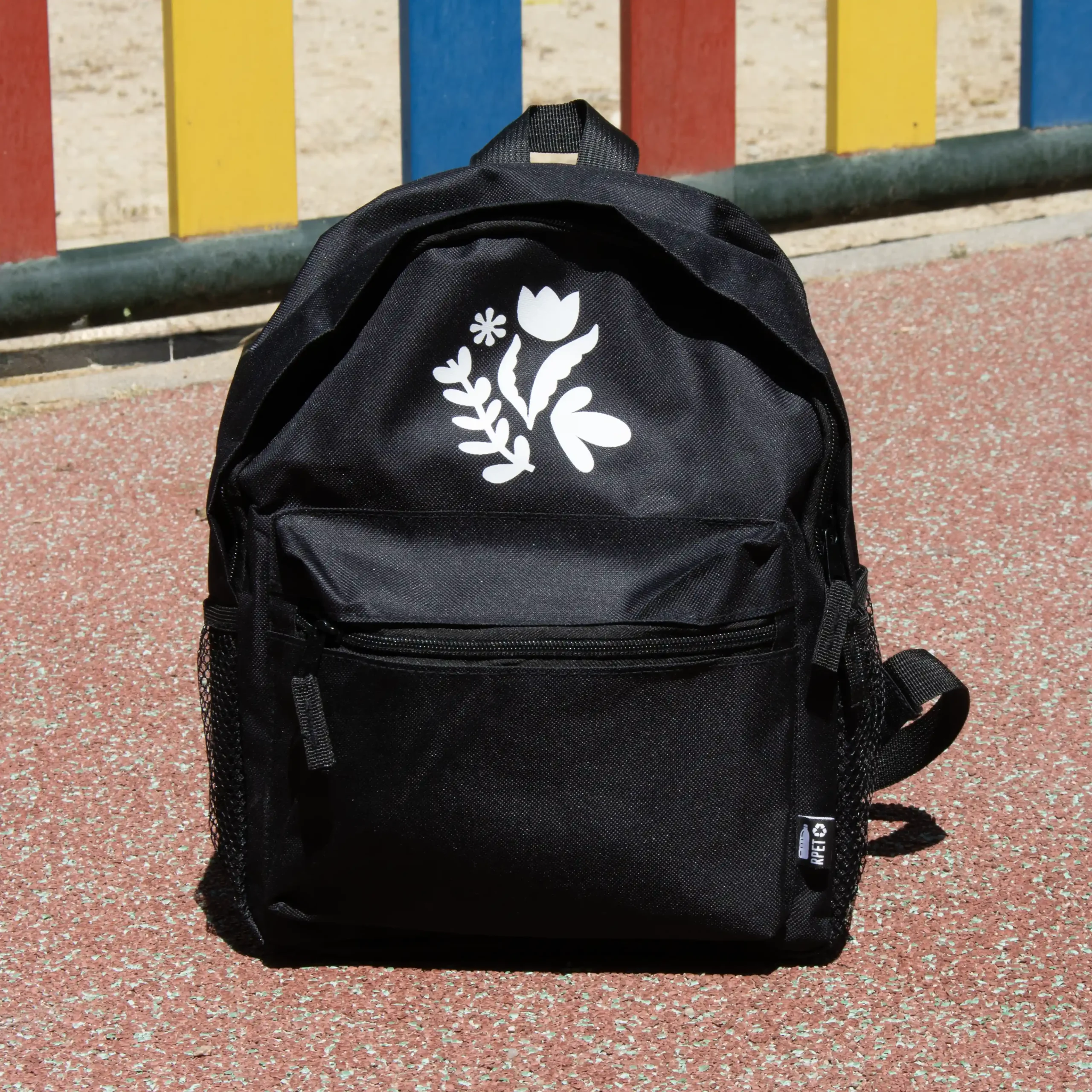 Mochila personalizada para niños color negro con logo blanco fondo suelo parque infantil