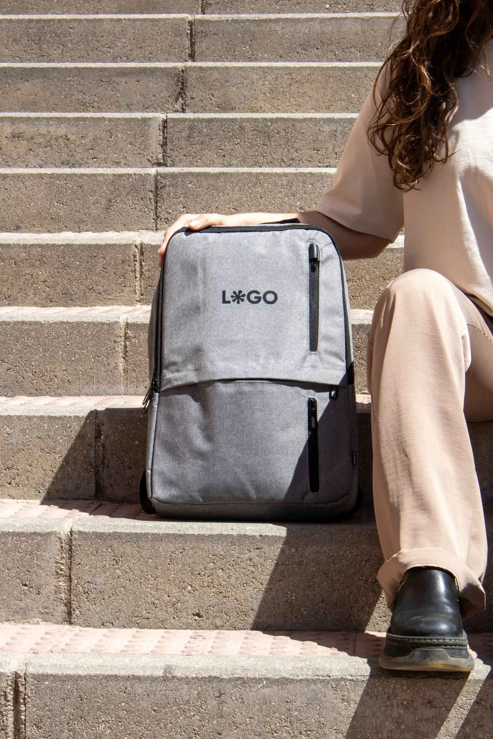 Sac à dos d'entreprise personnalisé gris avec logo noir modèle fille assise sur les marches de la rue