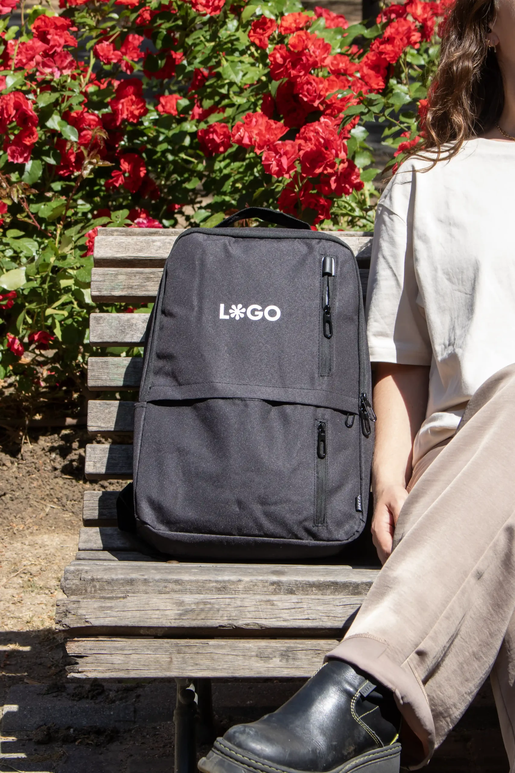 Sac à dos d'entreprise personnalisé noir avec logo blanc, modèle fille assise sur un banc de parc