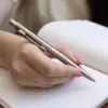 Mano escribiendo en cuaderno con bolígrafo de acero inoxidable personalizado