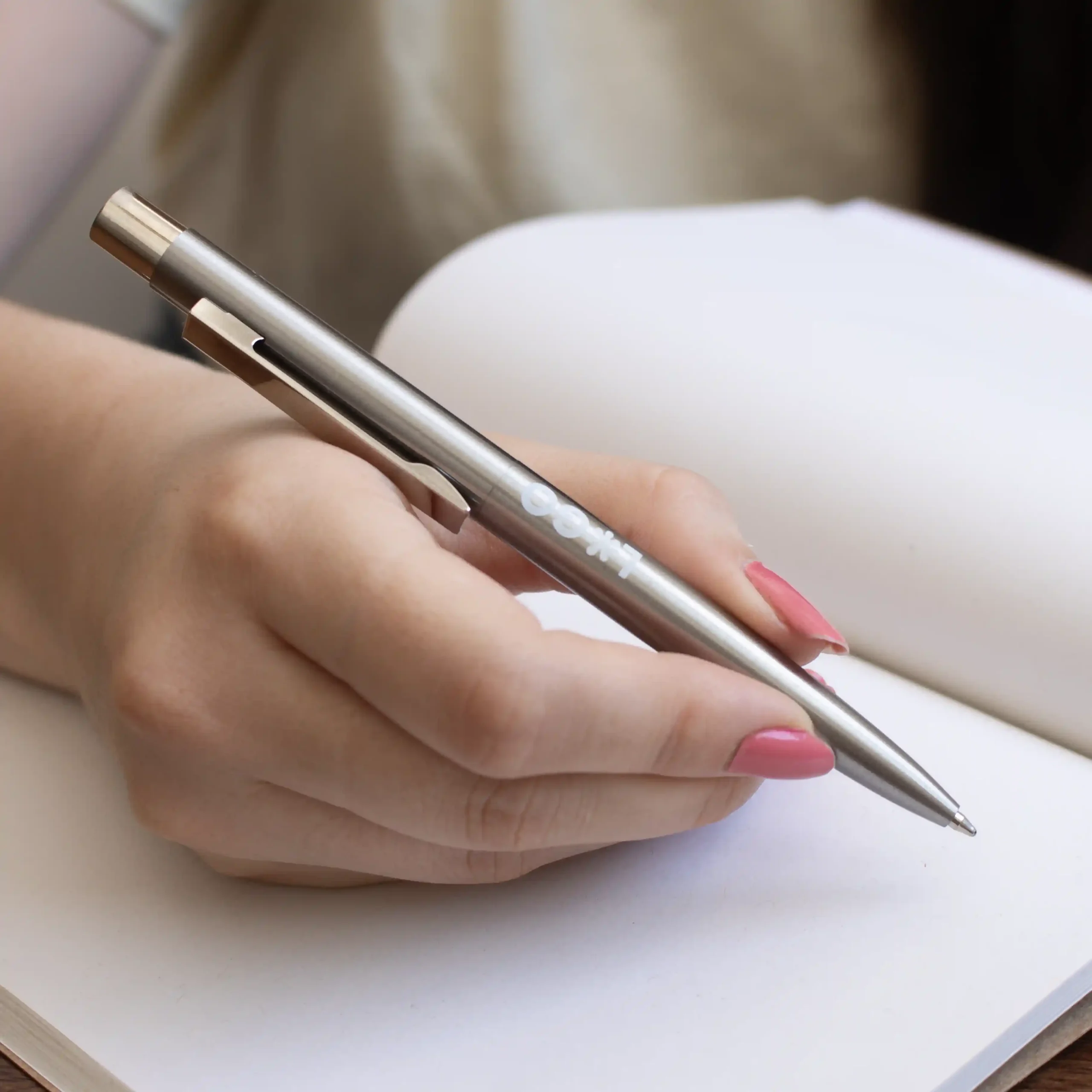 Mano escribiendo en cuaderno con bolígrafo de acero inoxidable personalizado