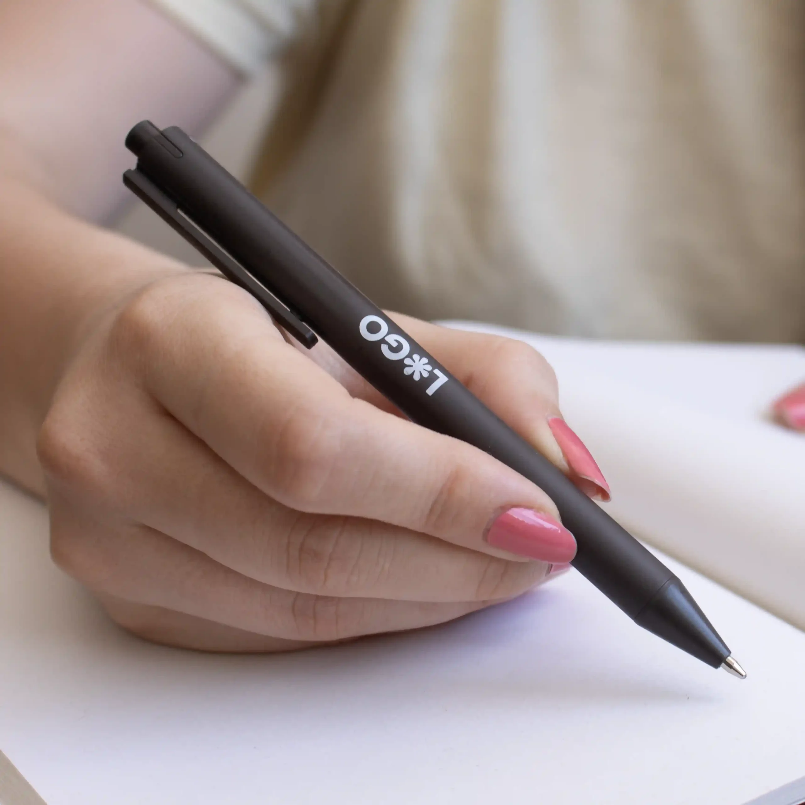 Mano escribiendo en cuaderno con bolígrafo de fibra de cafe personalizado con logo blanco