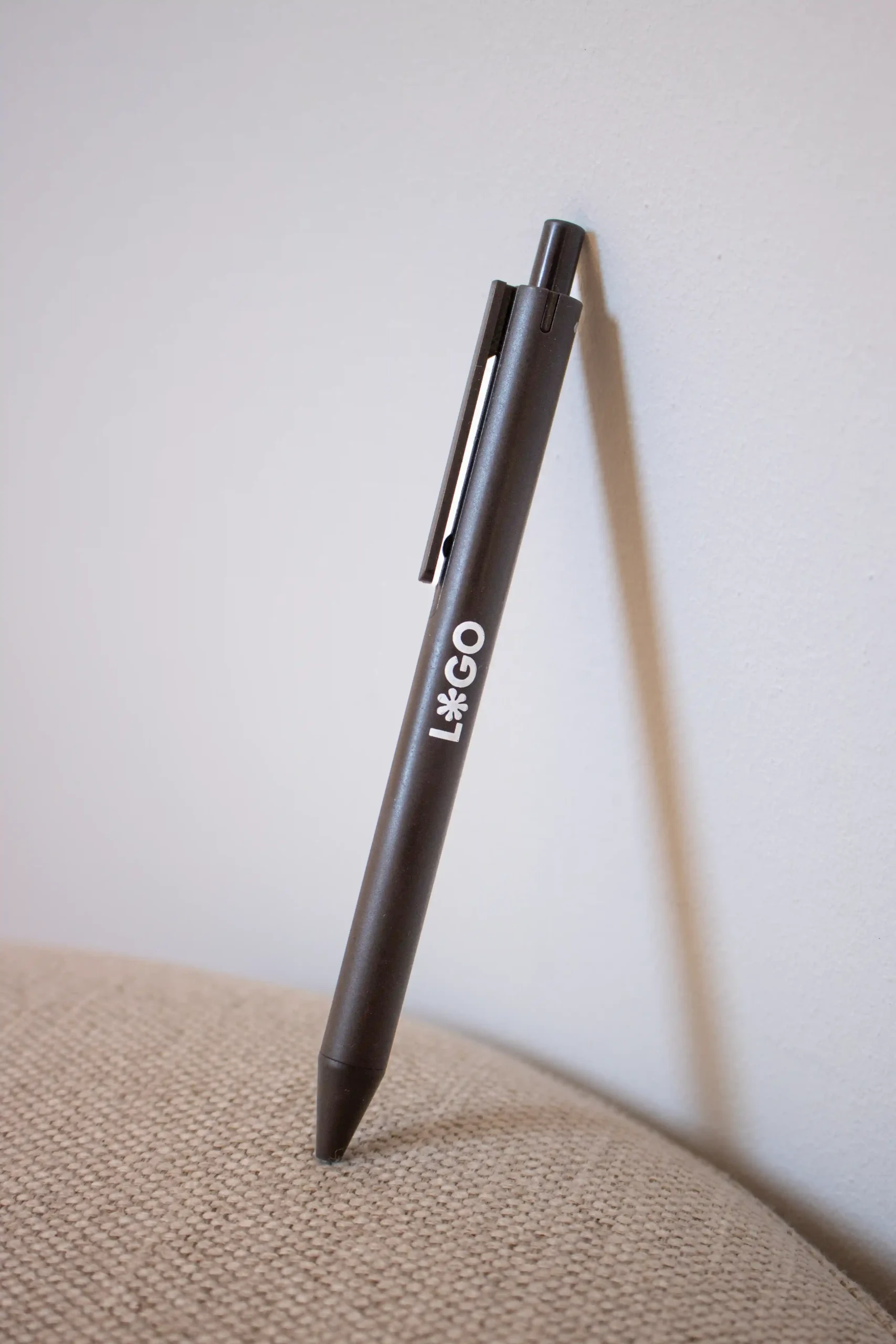 Bolígrafo marrón de fibra de cafe personalizado con logo blanco apoyado en la pared