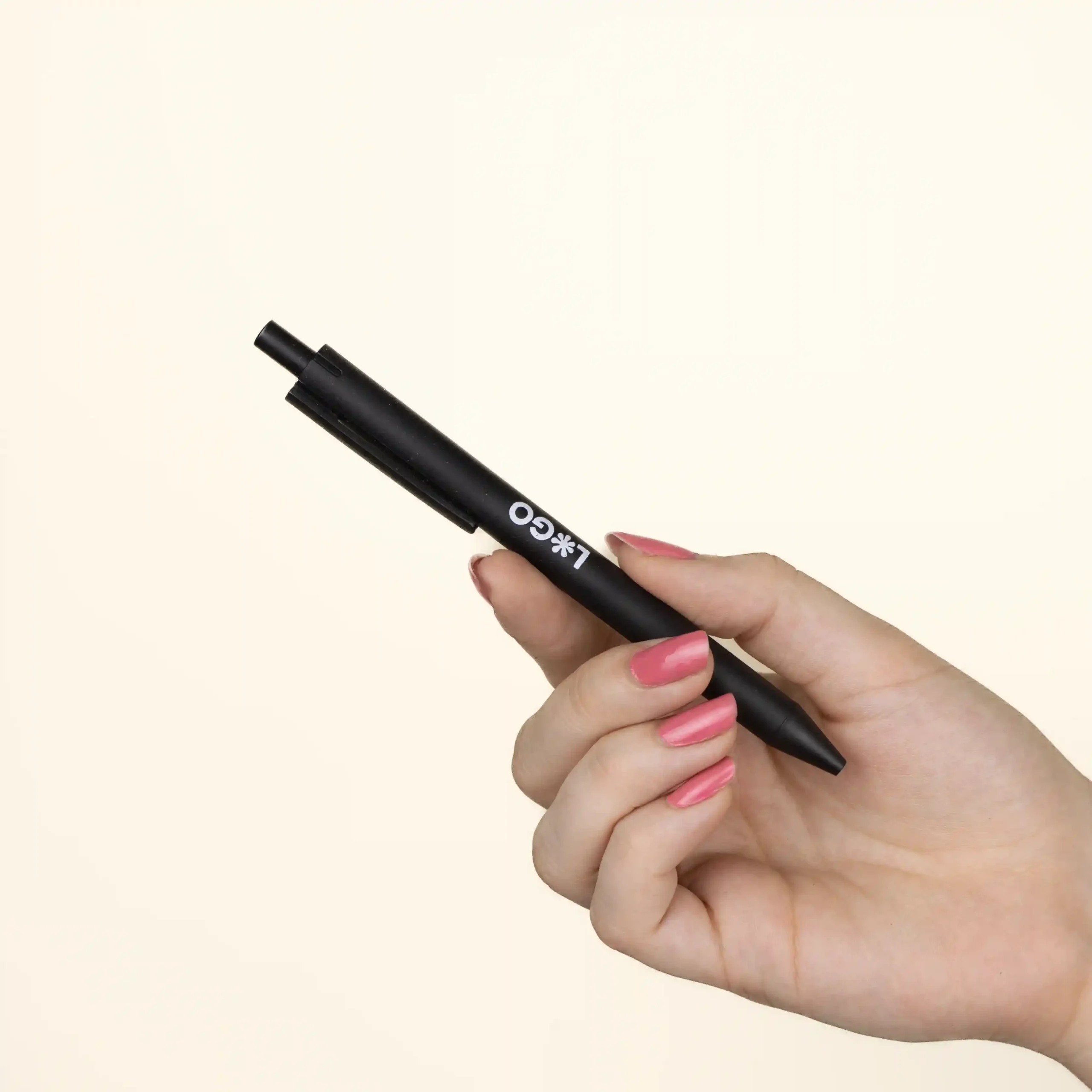 Bolígrafo trigo GLUT NegroMano Mano sujetando bolígrafo de caña de trigo negro personalizado con logo sobre fondo beige