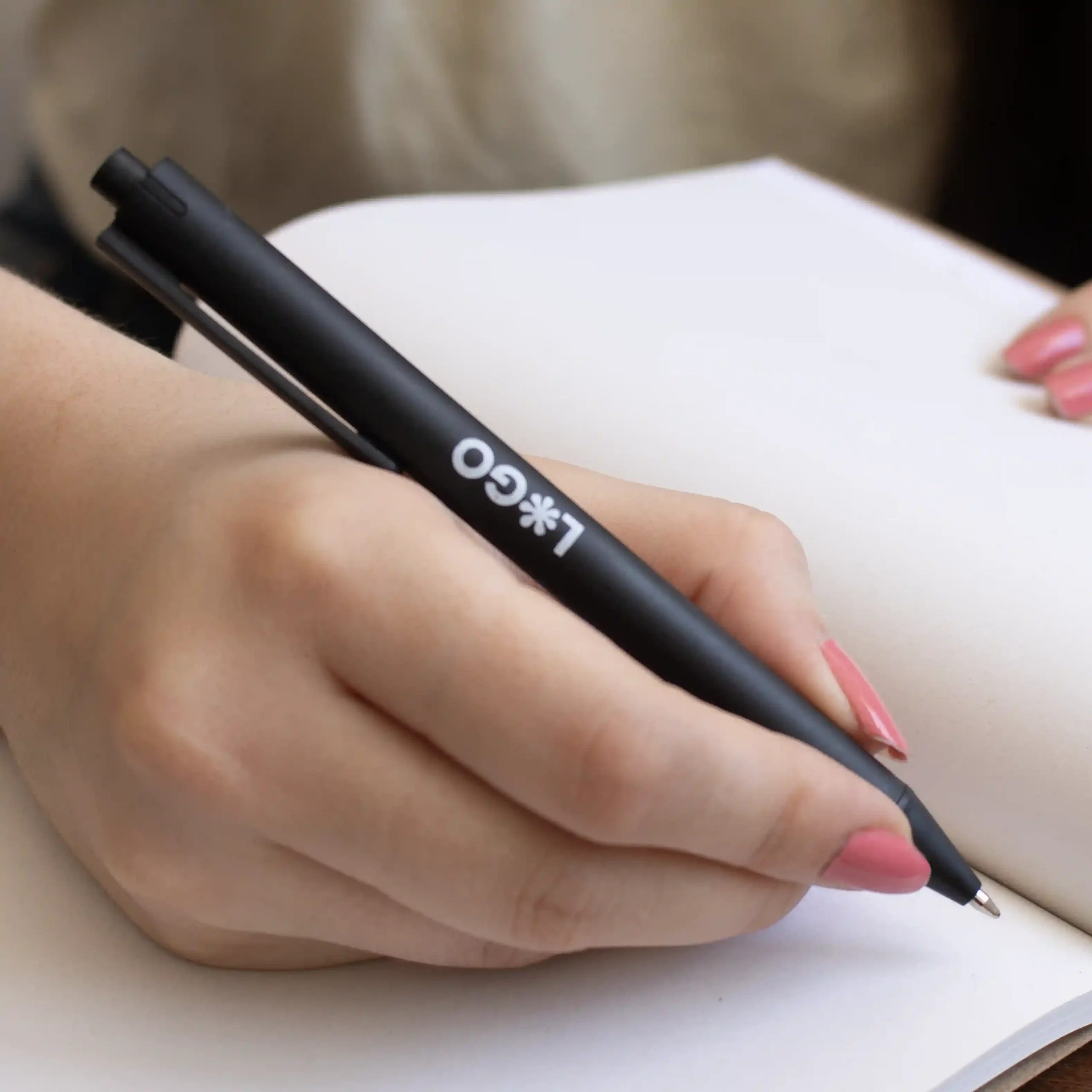 Mano escribiendo en cuaderno con bolígrafo de caña de trigo negro personalizado con logo