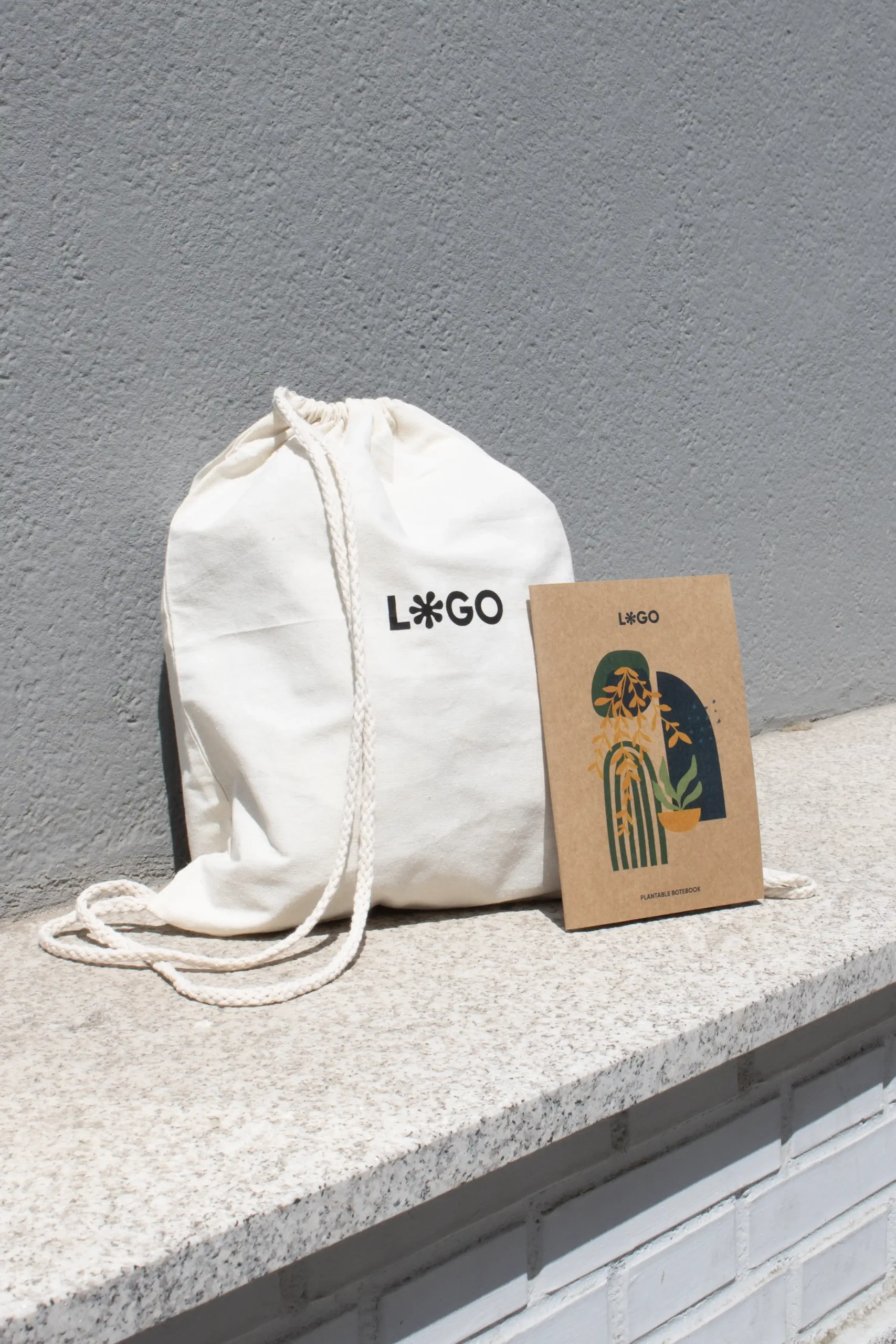 Mochila cuerdas personalizada tipo saco color beige con logo negro y cuaderno con portada kraft