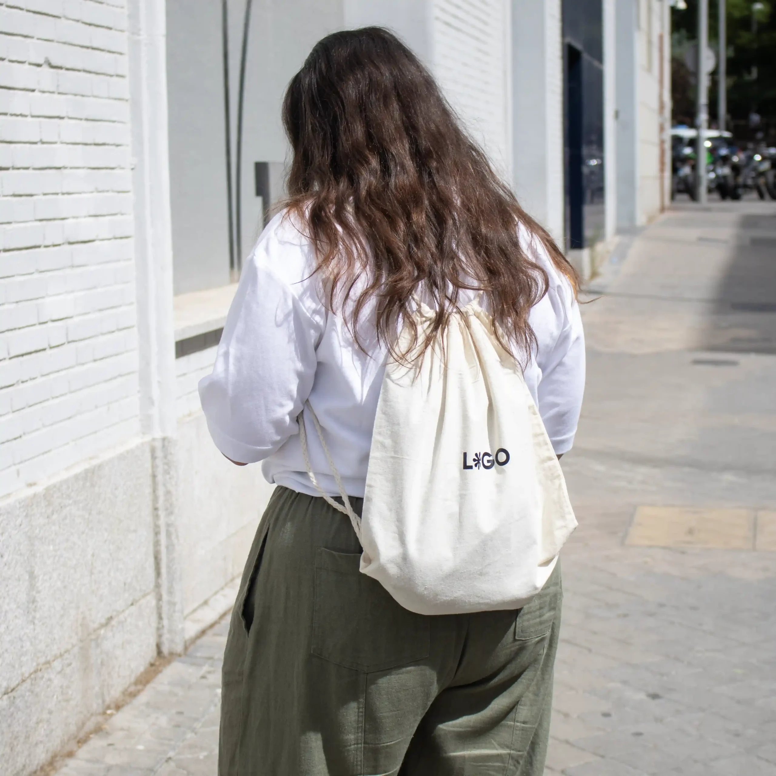 Mochila cuerdas personalizada tipo saco color beige con logo negro modelo chica caminando en la calle