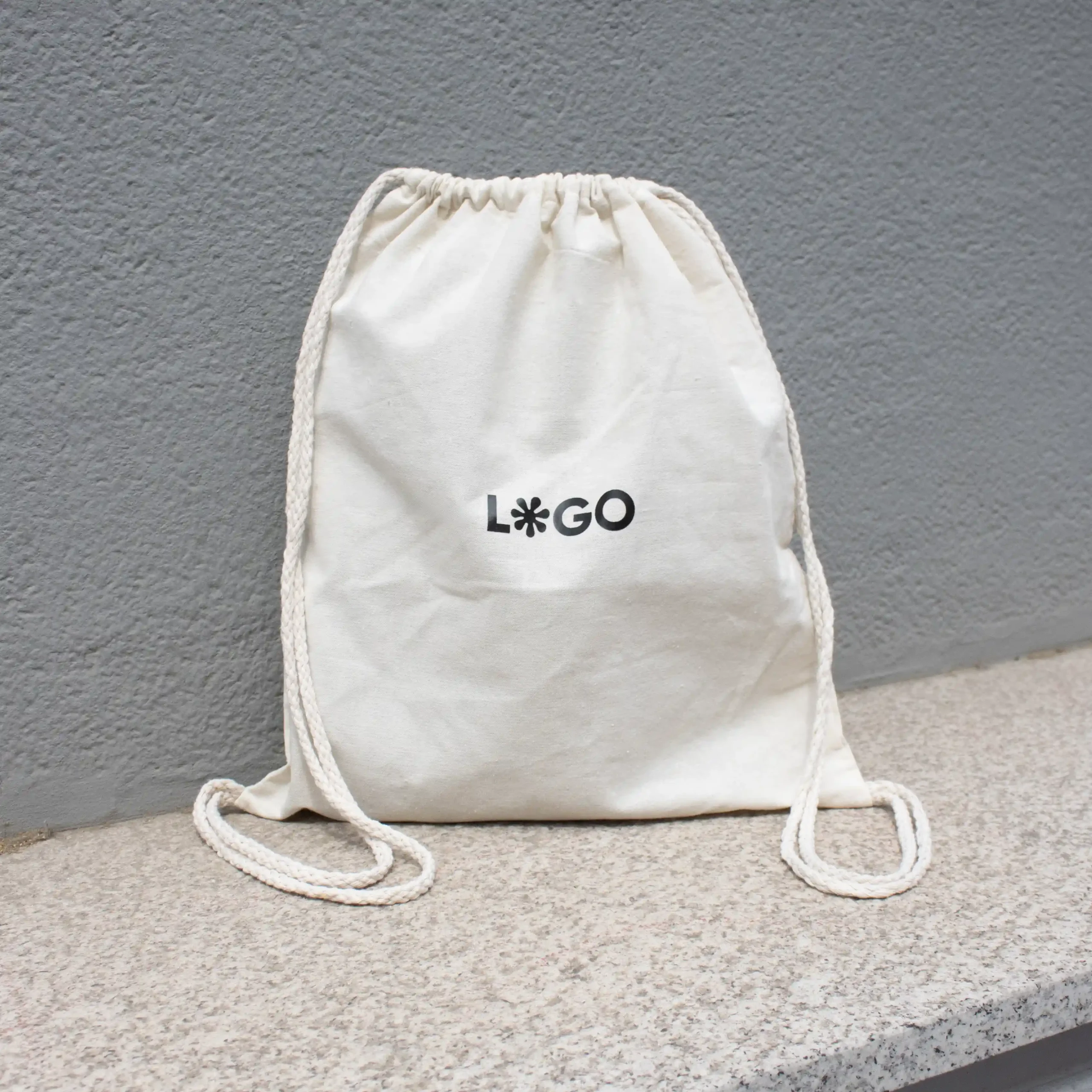 Mochila cuerdas personalizada tipo saco color beige con logo negro fondo gris