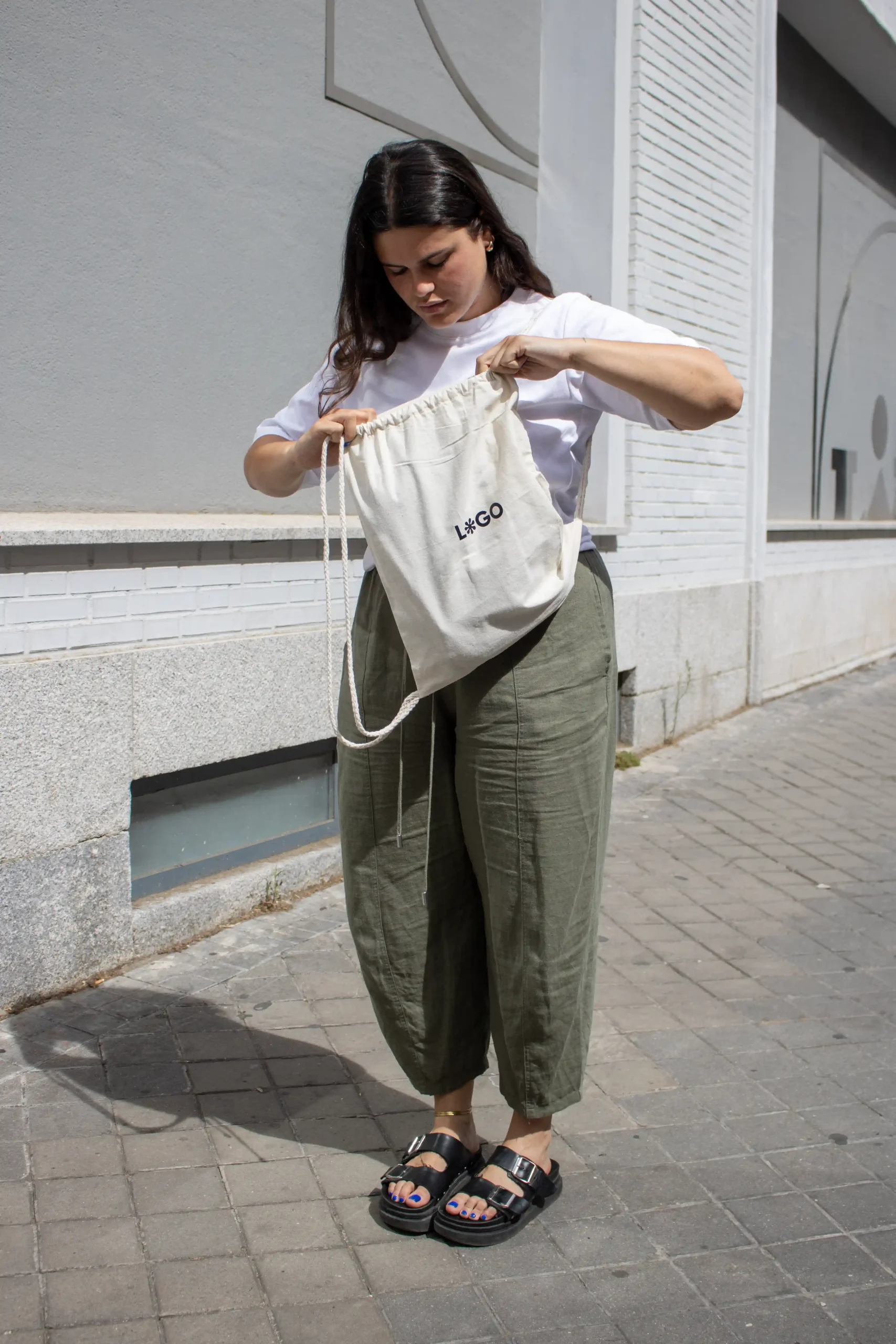 Mochila cuerdas personalizada tipo saco color beige con logo negro modelo chica abriendo la mochila