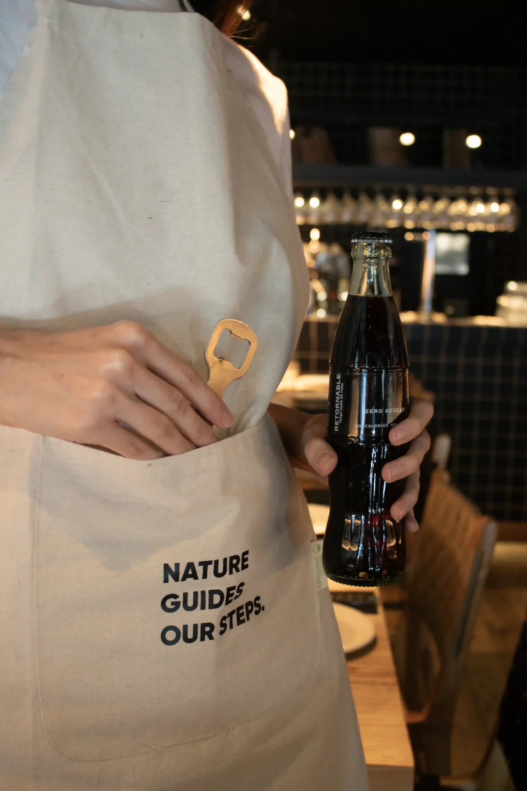 Delantal algodón personalizado color natural modelo camarera abriendo refresco