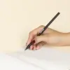 Lápiz de madera BRUNO Mano Mano escribiendo en cuaderno con lápiz de madera negro personalizado con logo blanco fondo beige