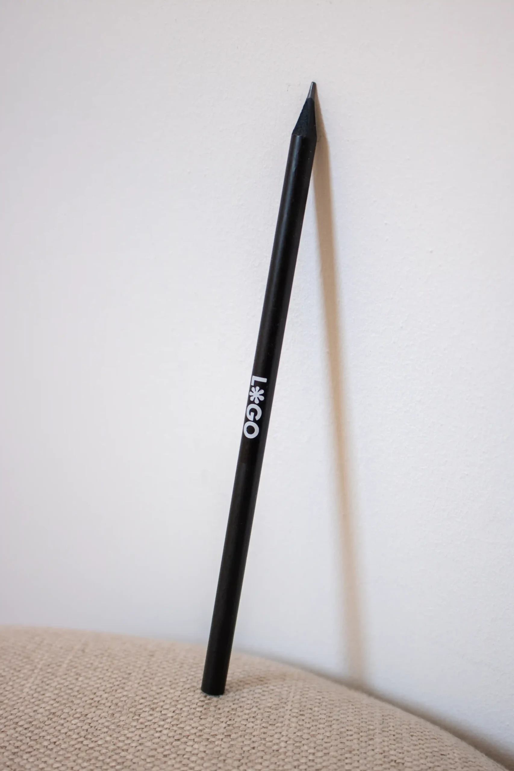 lápiz de madera negro personalizado con logo blanco apoyado en pared