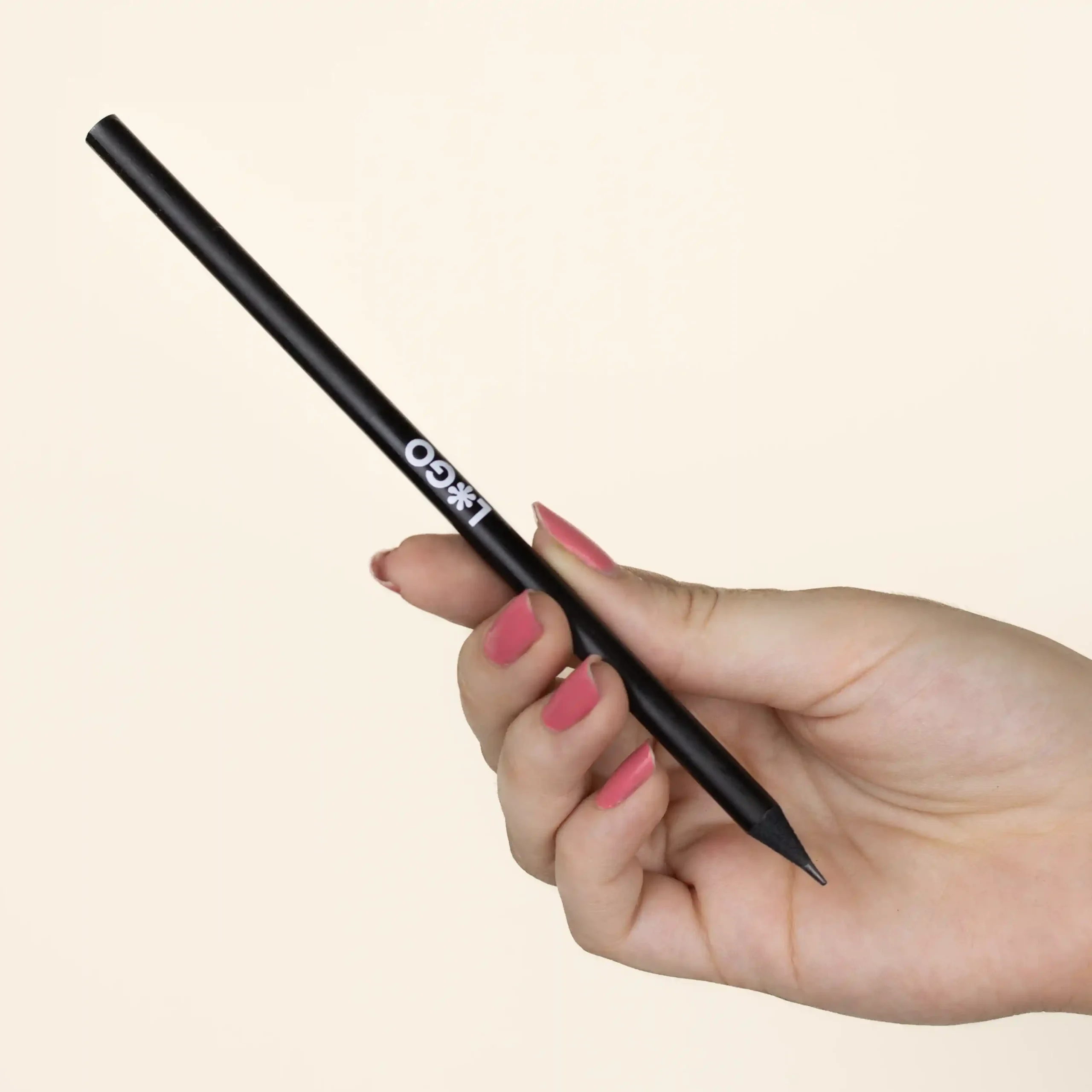 Mano sujetando un lápiz de madera negro personalizado con logo blanco fondo beige