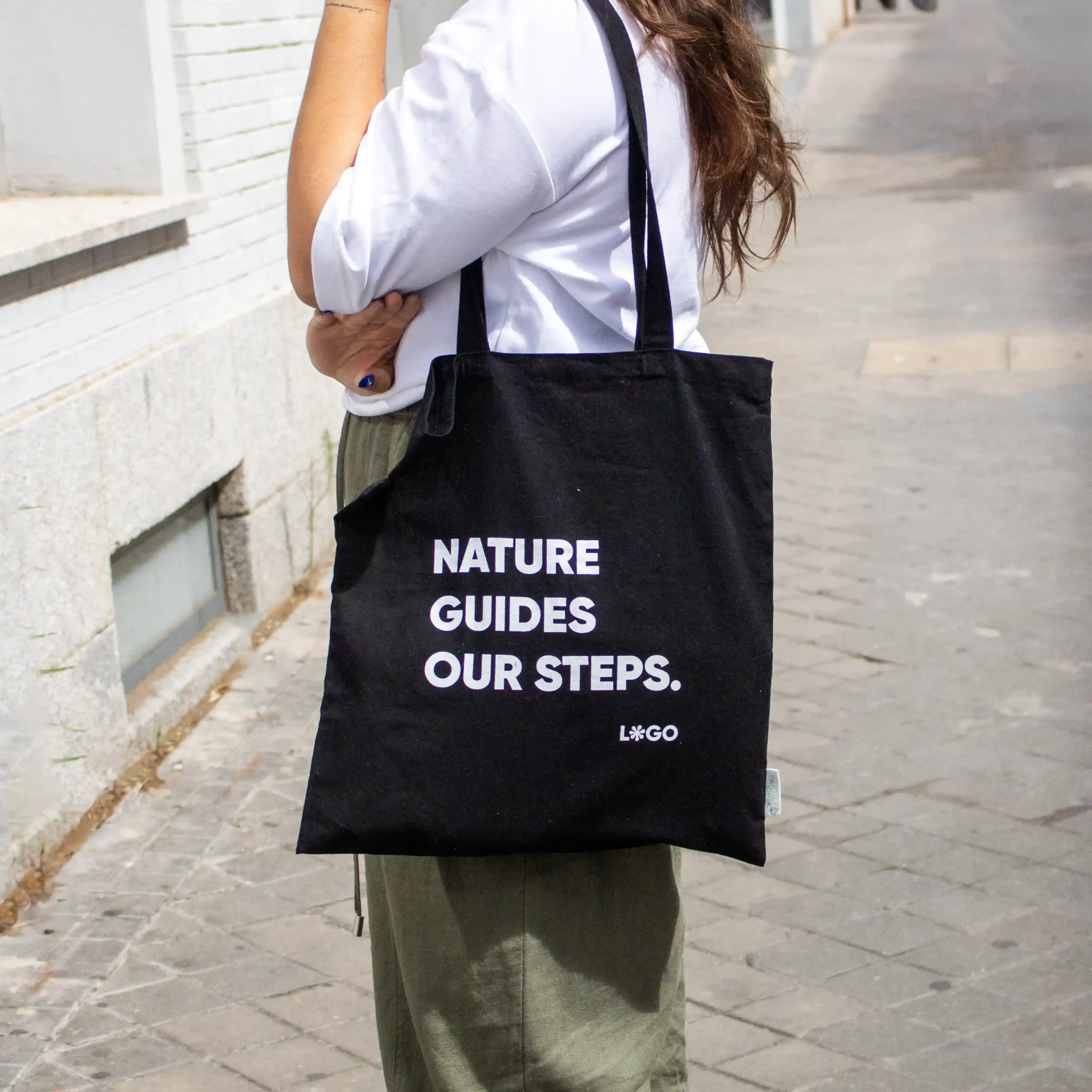 Chica en la calle llevando una bolsa negra de algodón orgánico personalizada con logo blanco