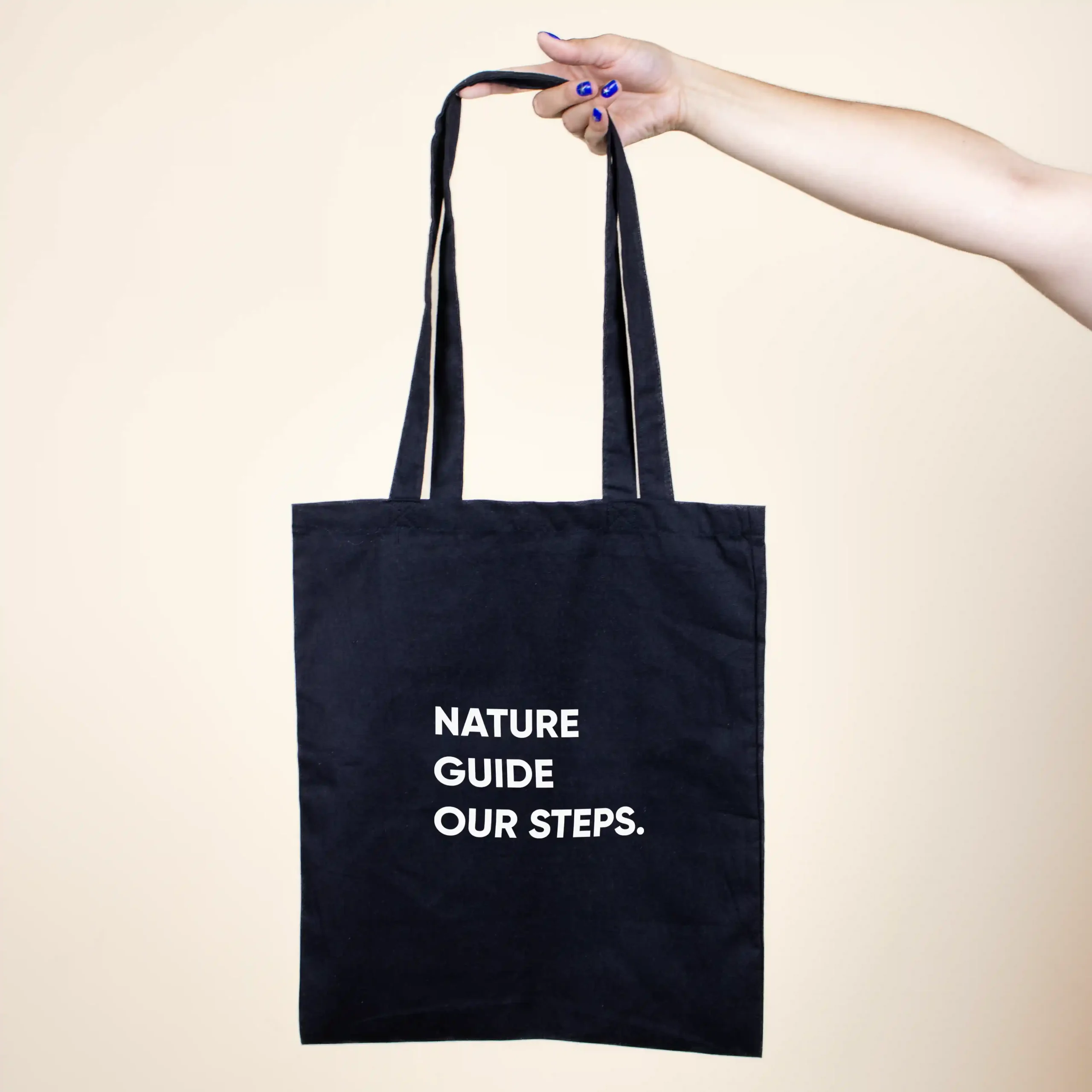 Mano sujetando una bolsa negra de algodón orgánico personalizada con logo blanco