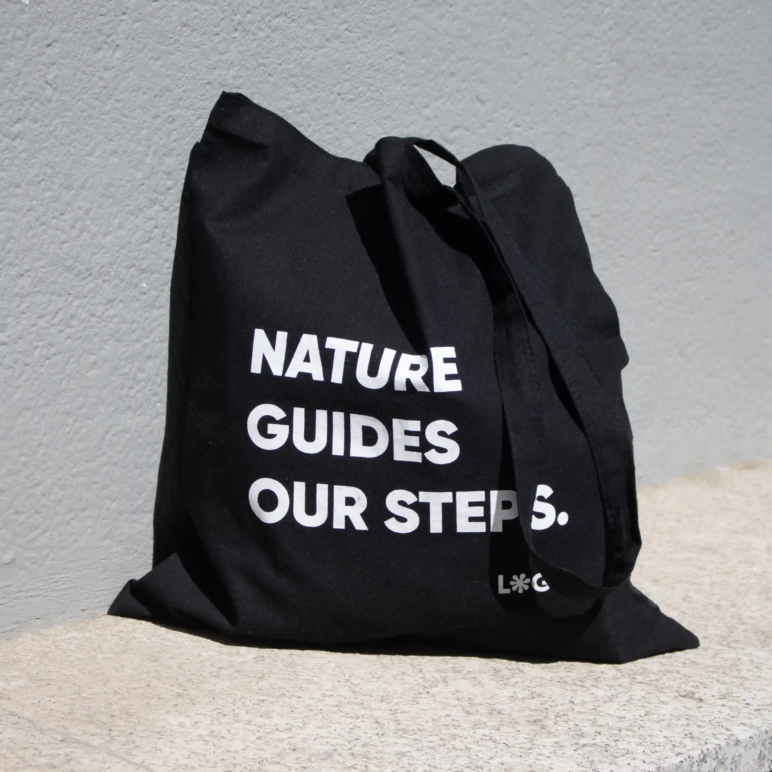 Bolsa negra de algodón orgánico personalizada con logo blanco apoyada en el suelo