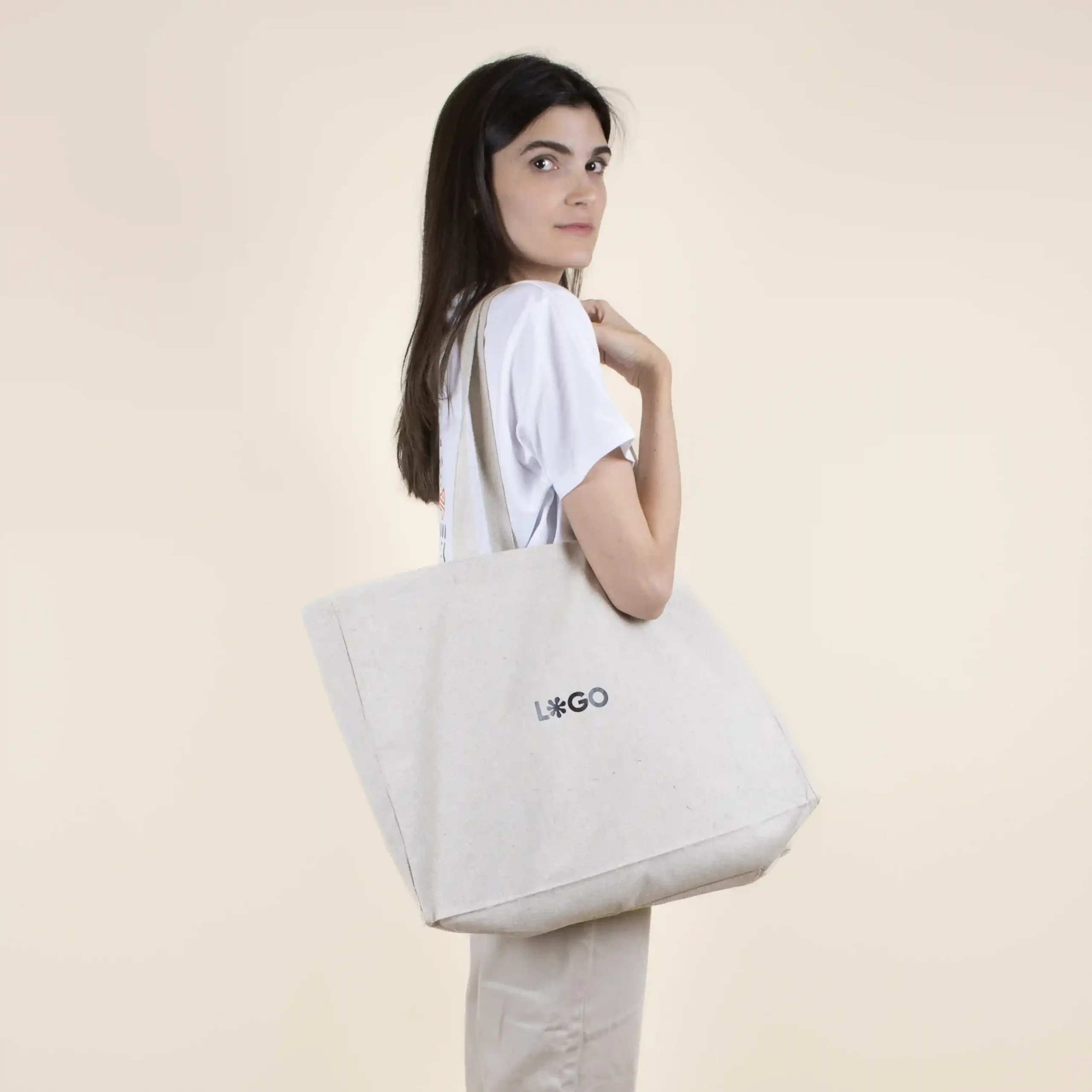 Chica sobre fondo beige con bolsa de algodón reciclado personalizada con logo