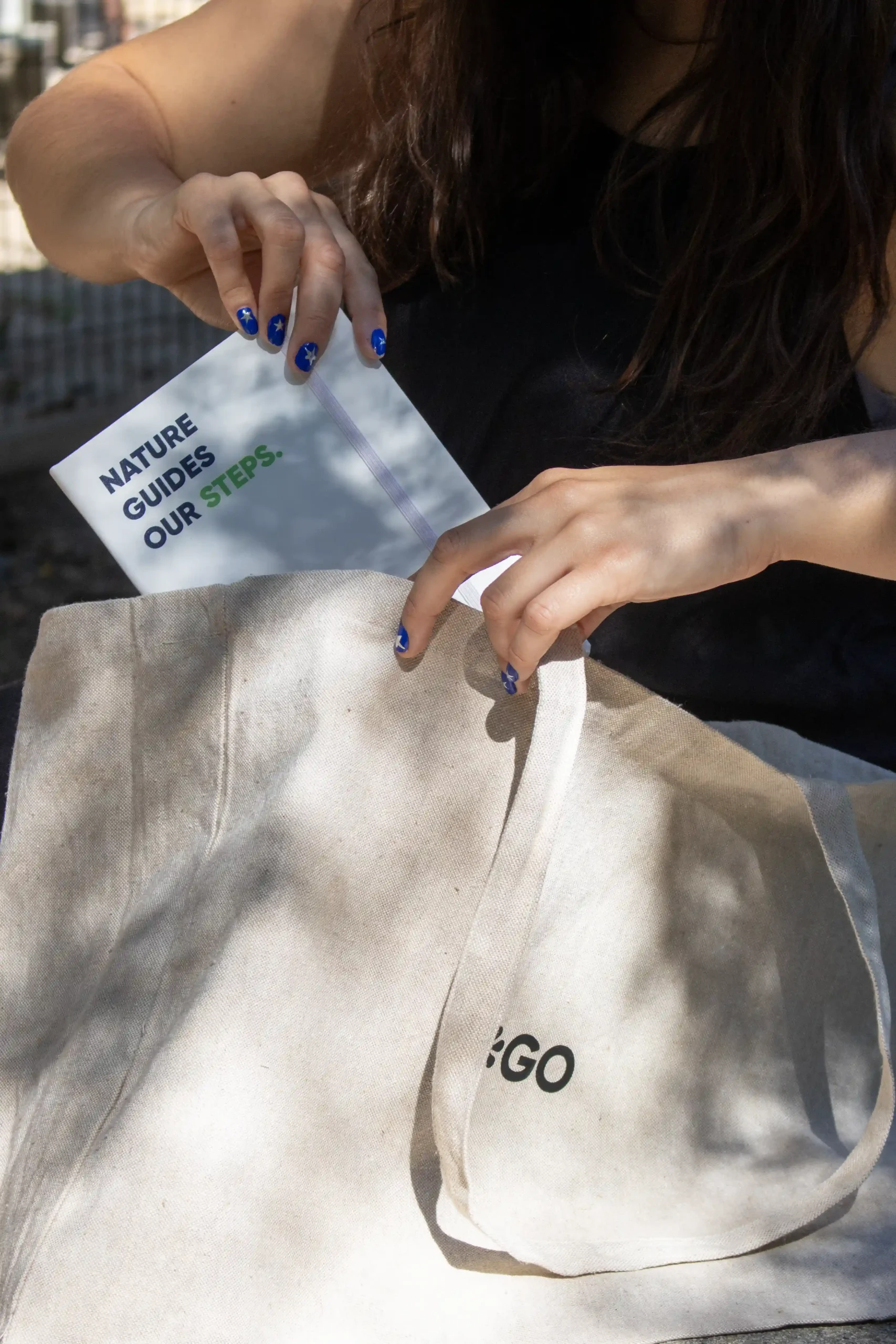 Manos de chica sacando un cuaderno de una bolsa de algodón reciclado personalizada con logo