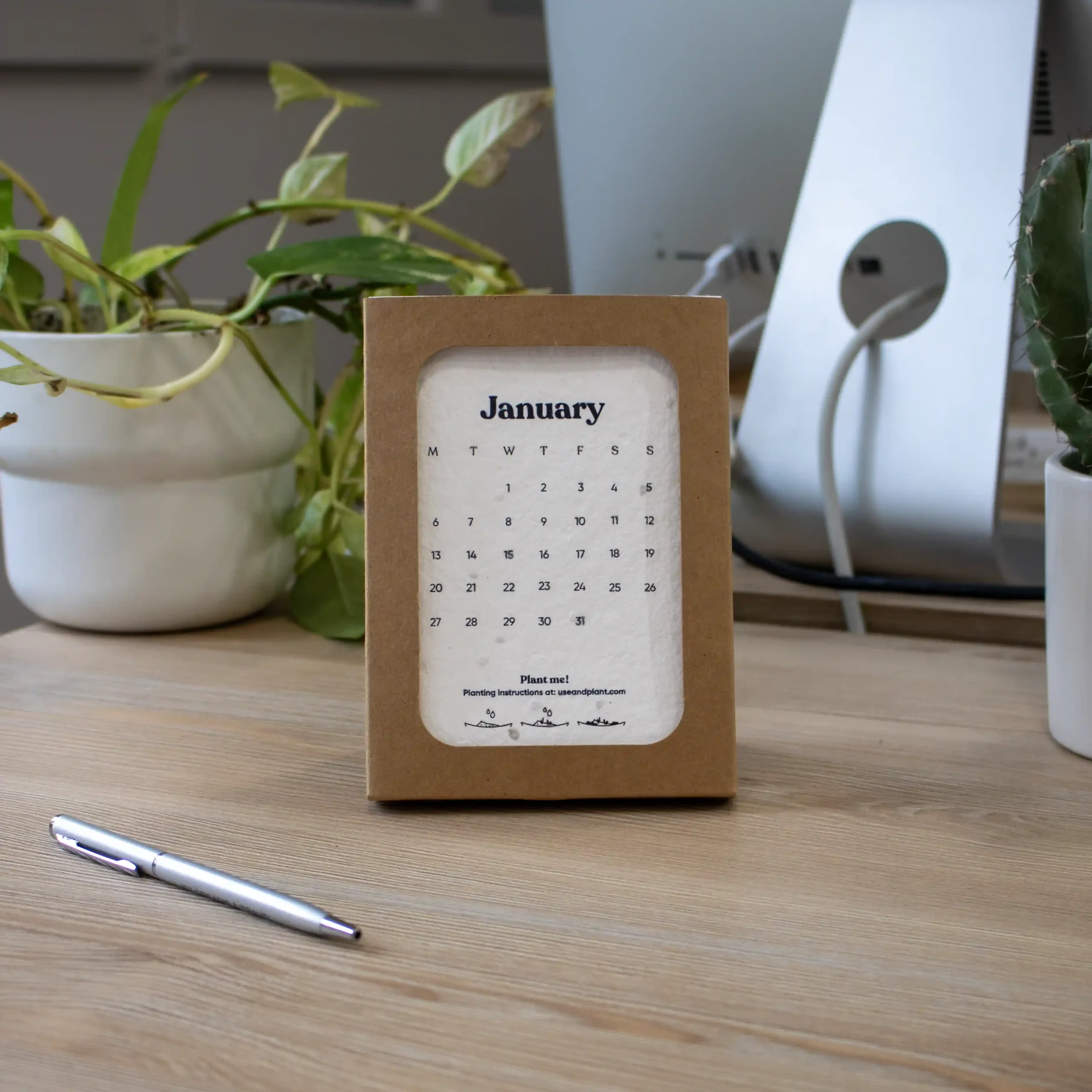 Calendario de semillas en estuche kraft personalizado colocado en una mesa de trabajo con un bolígrafo y un ordenador