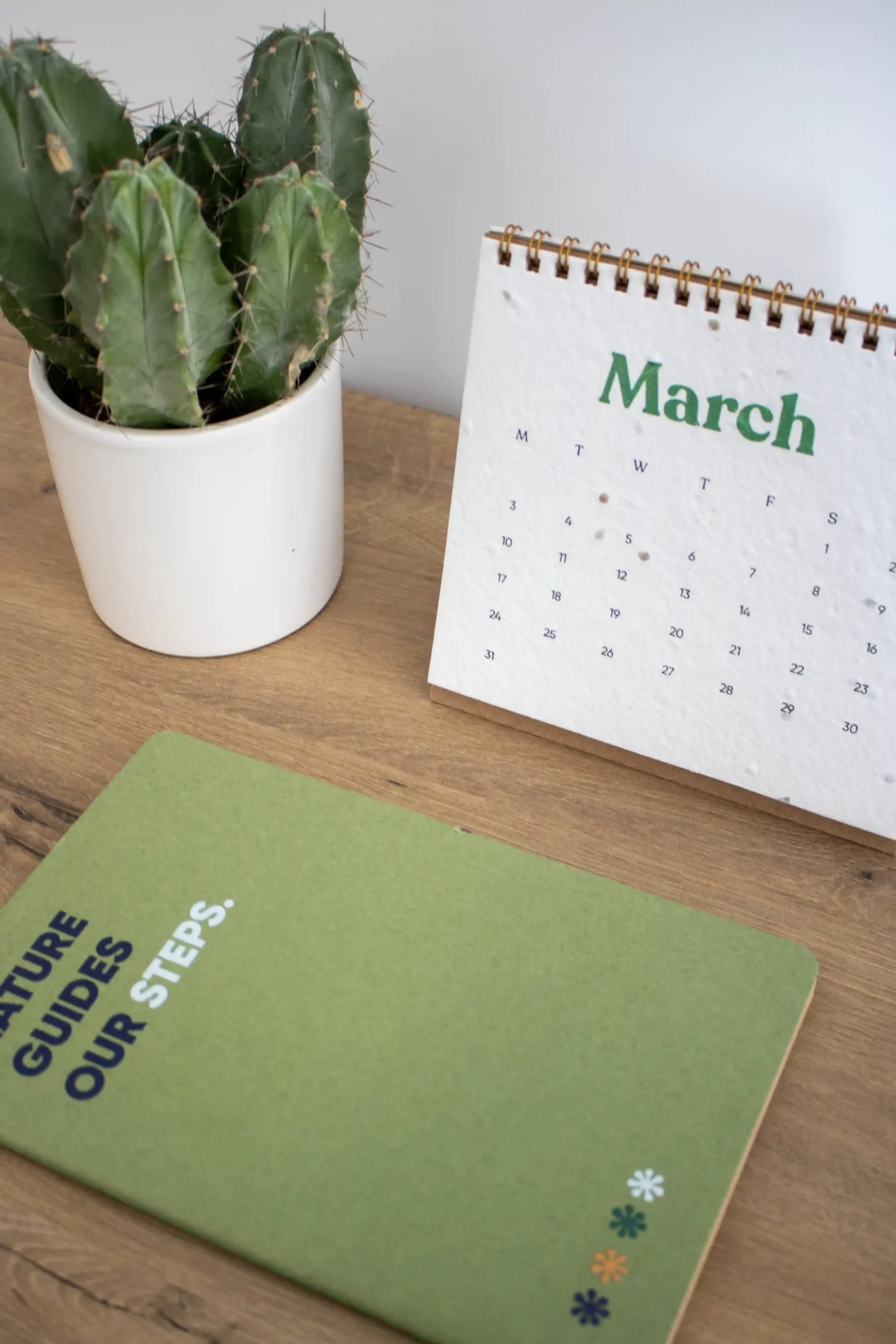 Calendario plantable de mesa abierto en el mes de marzo sobre una mesa de madera con un cuaderno verde y un cactus