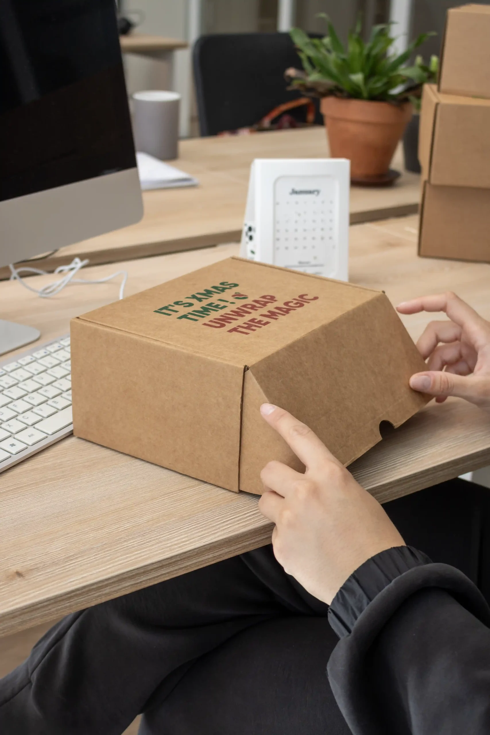 Manos abriendo una caja regalo de Navidad personalizada sobre una mesa de trabajo
