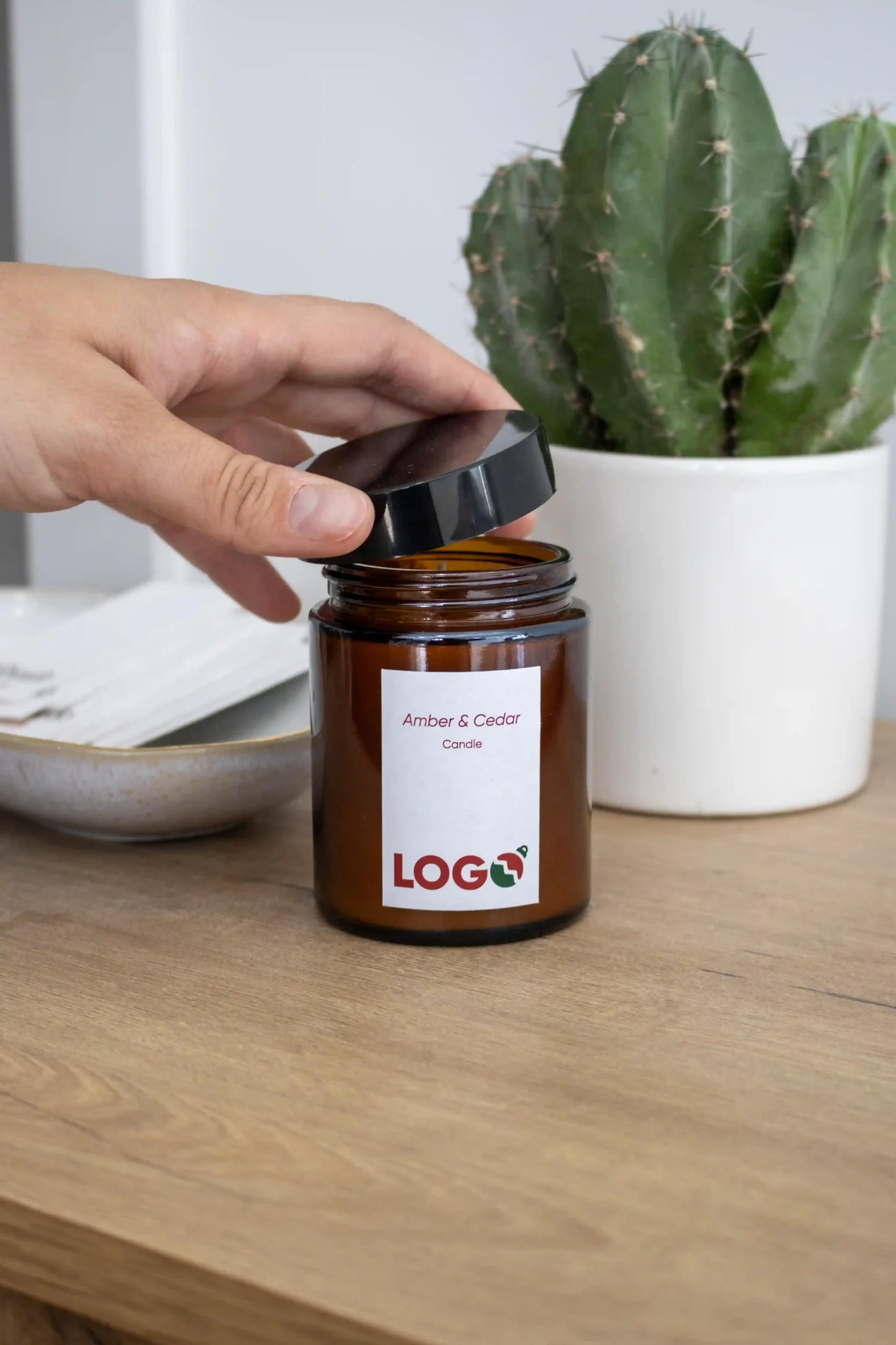 Mano abriendo una vela personalizada con diseño de Navidad acompañada de un cactus sobre una mesa de madera