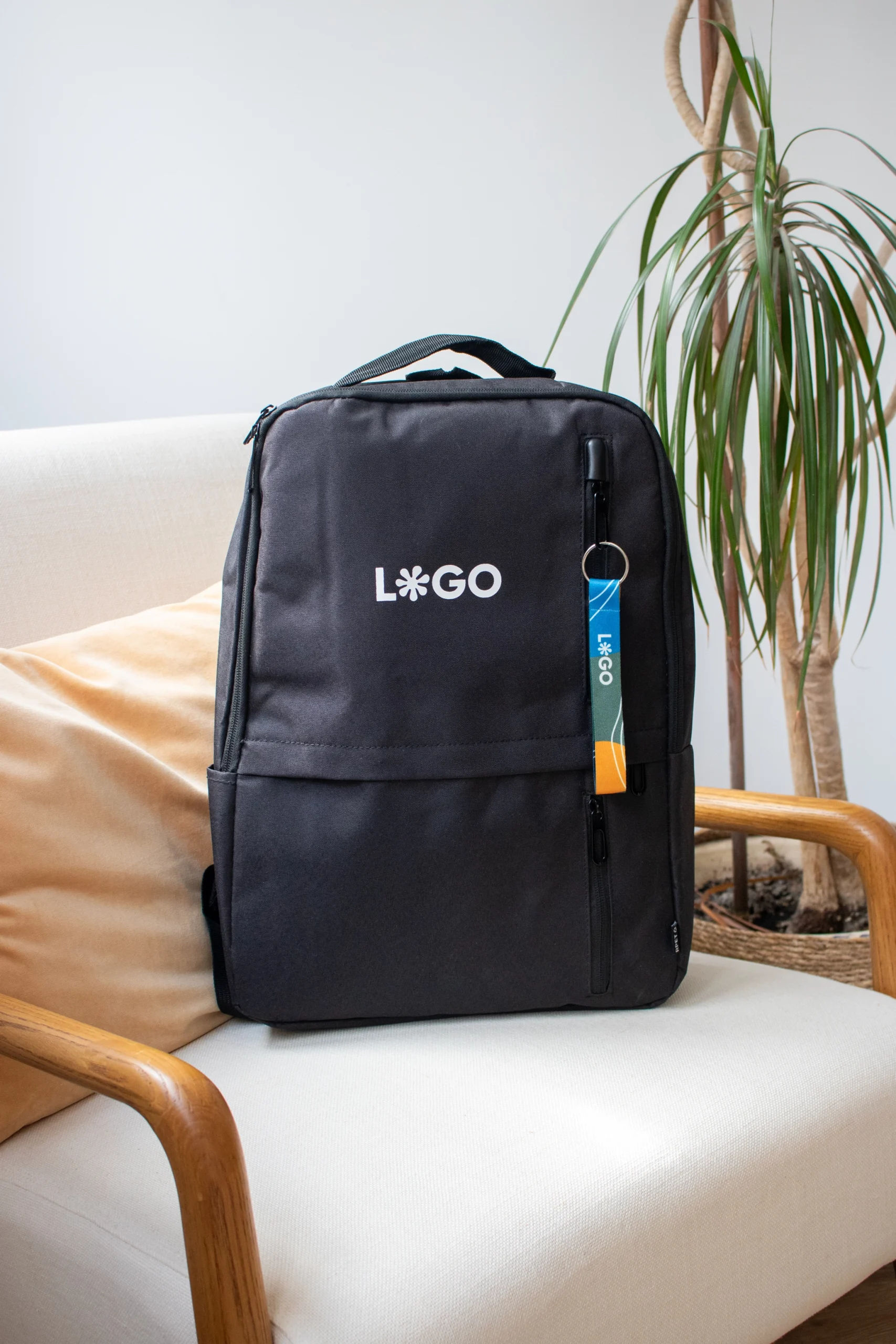 Mochila negra con un llavero ecológico personalizado con logo sobre un sillón